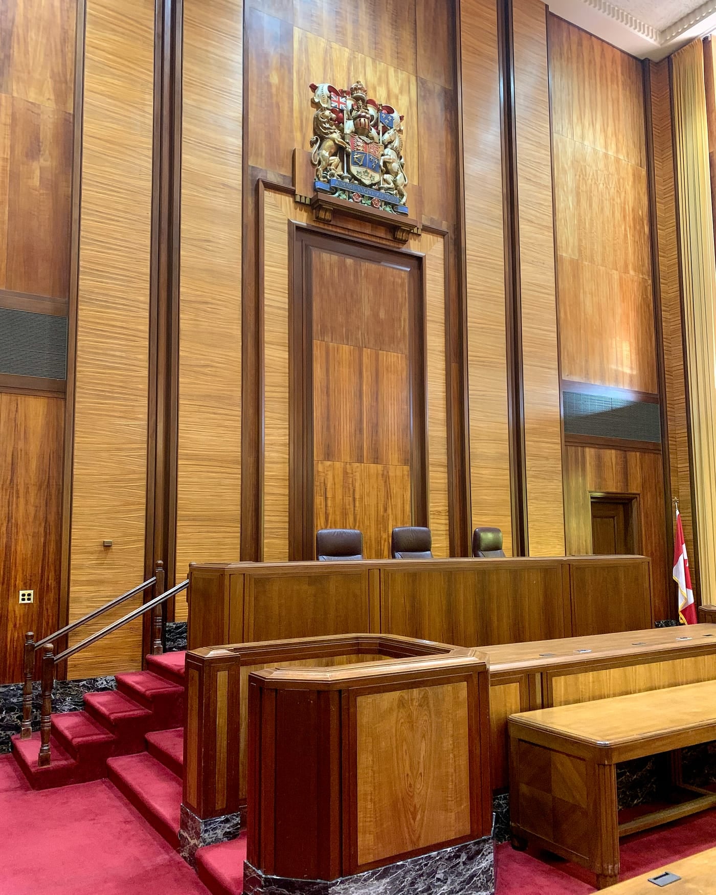 Wood-panelled federal courtroom with judges bench, coat of arms, red carpet and empty seats
