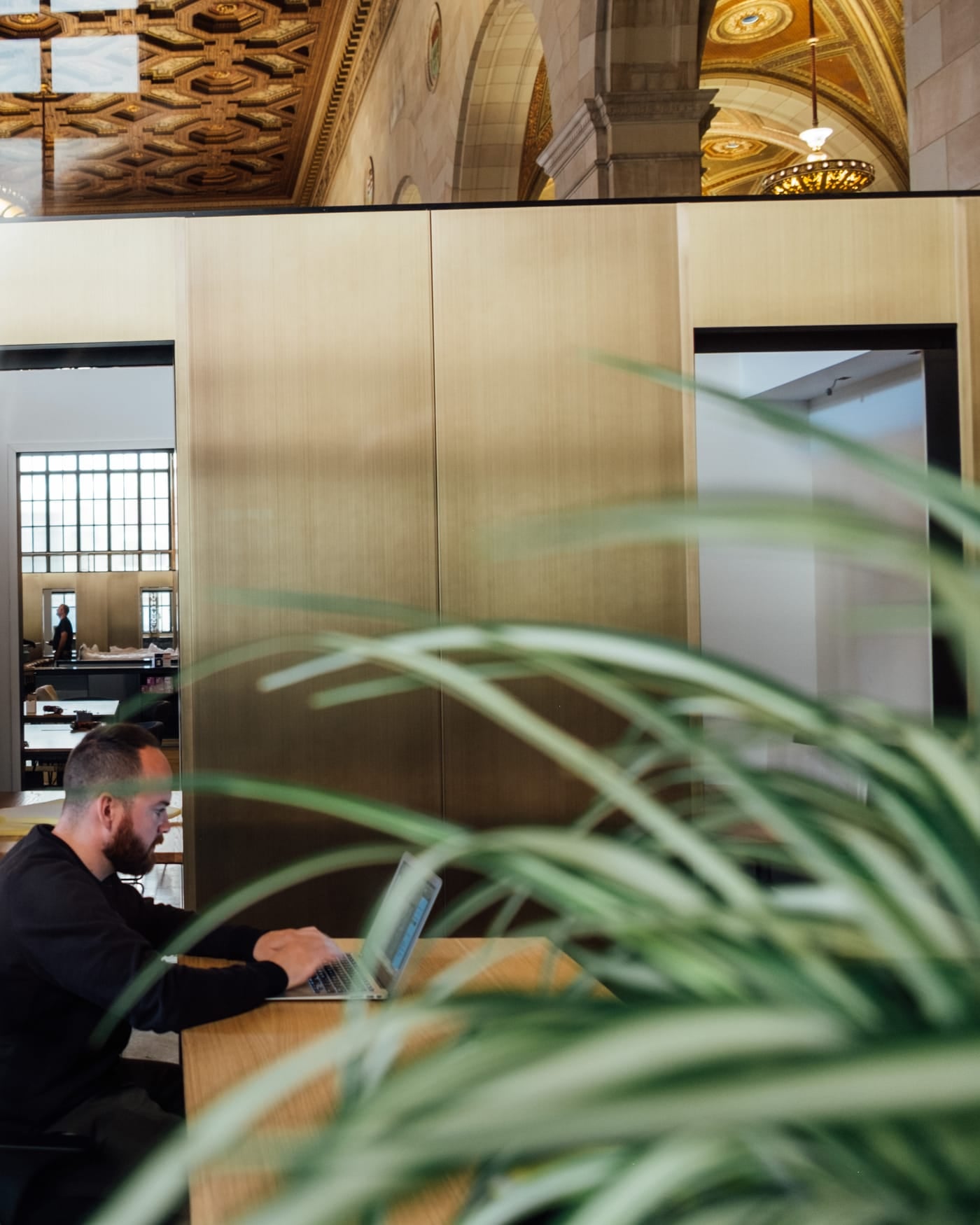 Man working at a laptop behind brass-framed glass partitions in an open-plan office