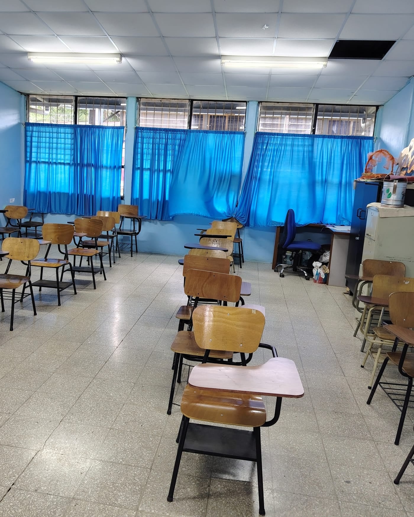 Empty classroom with wooden desks, blue walls and blue curtains on large windows