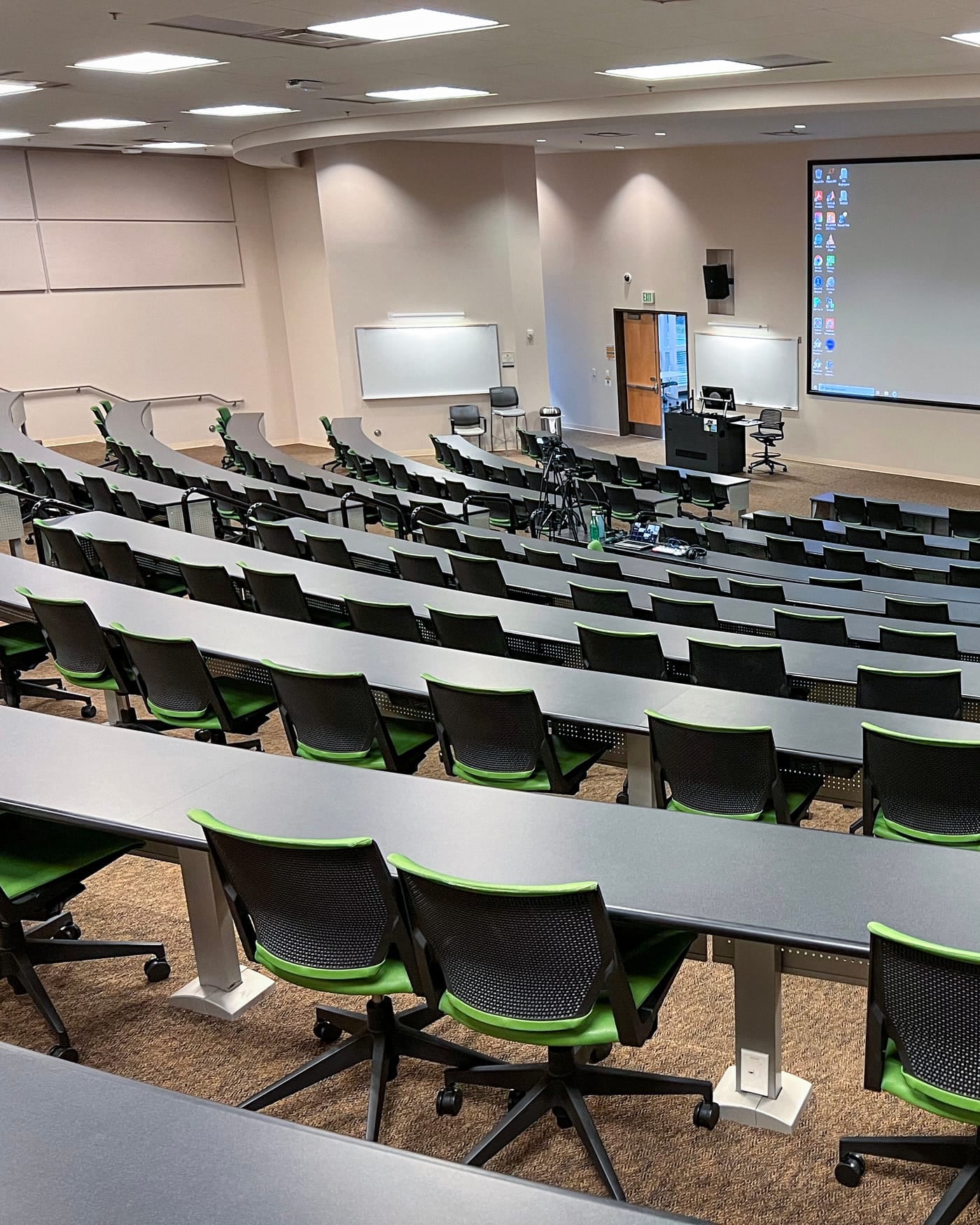 Modern tiered training room with rows of desks, green chairs and a projector screen