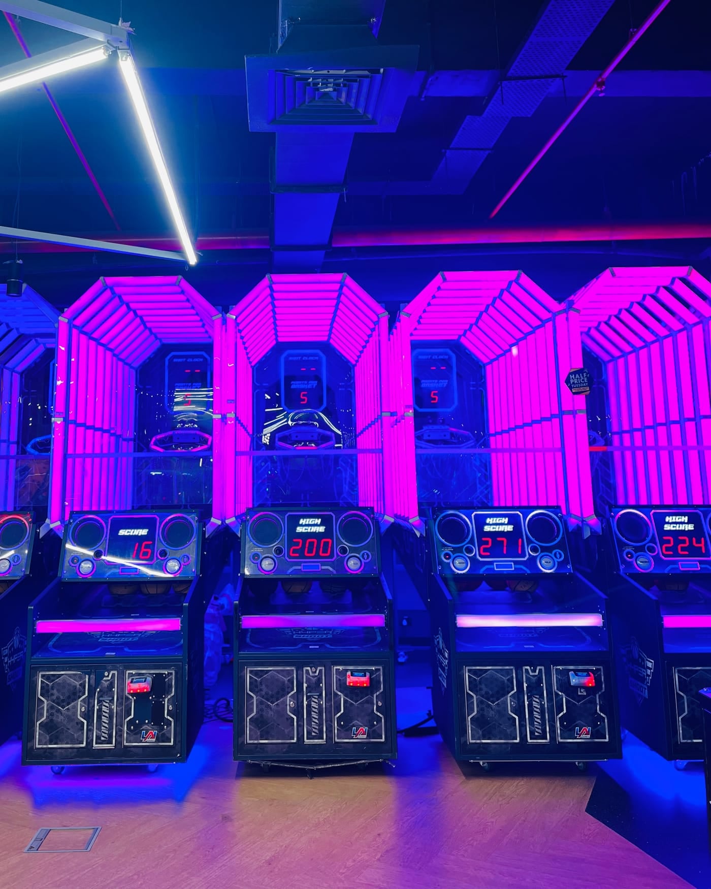 Row of arcade basketball machines glowing pink and blue under neon light