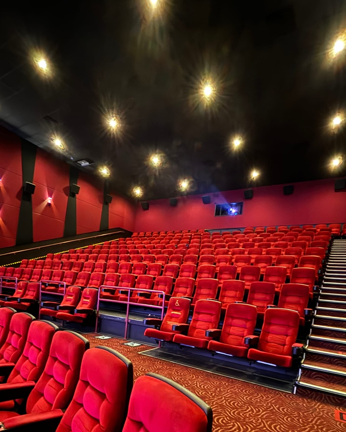 Empty movie theater auditorium with rows of red velvet seats and ceiling lights