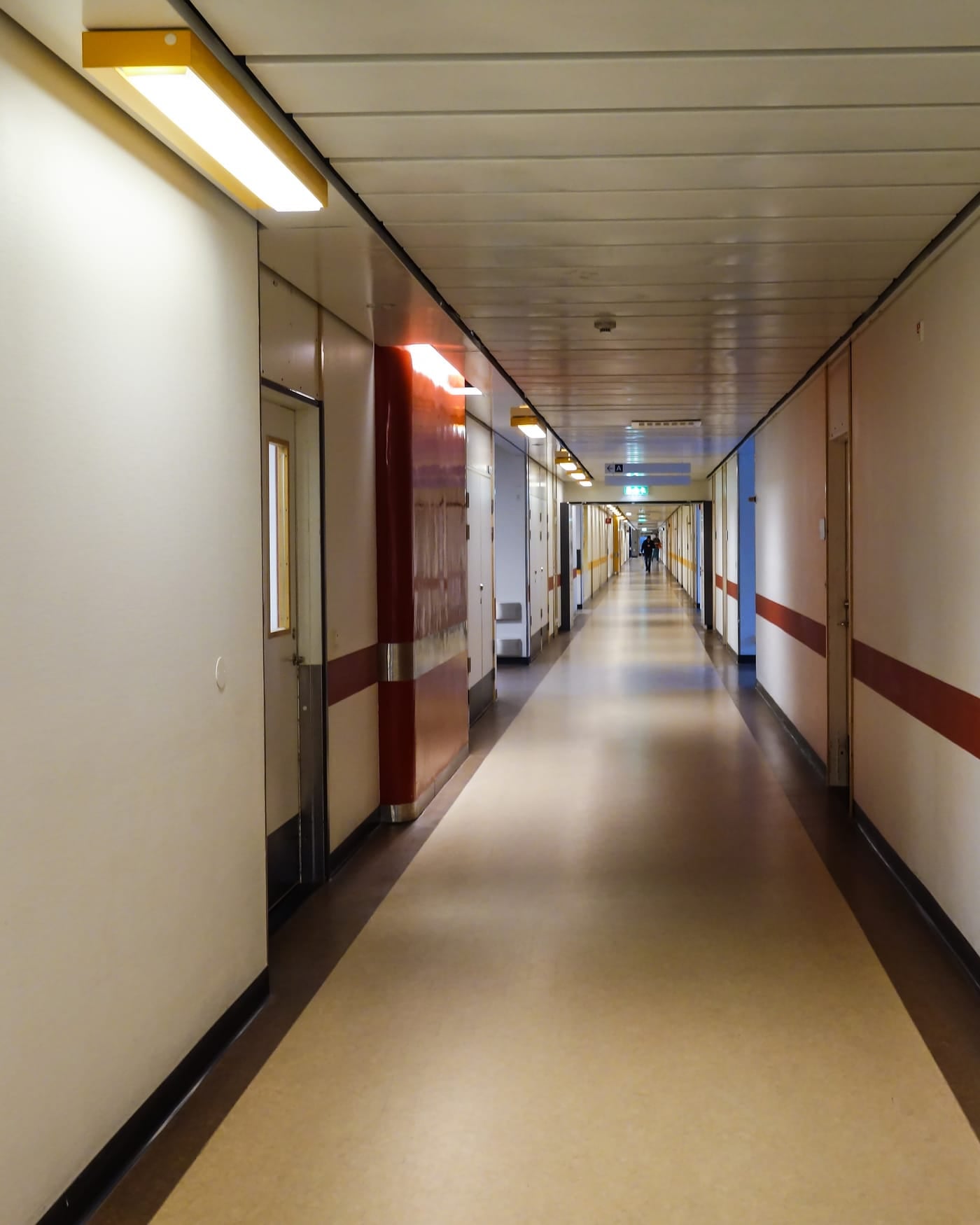 Long empty hospital corridor with pale walls, red door frames and a light floor