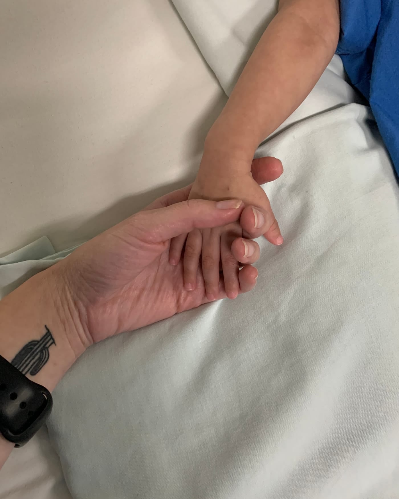A nurse's hand gently holding a patient's hand on white hospital bedding