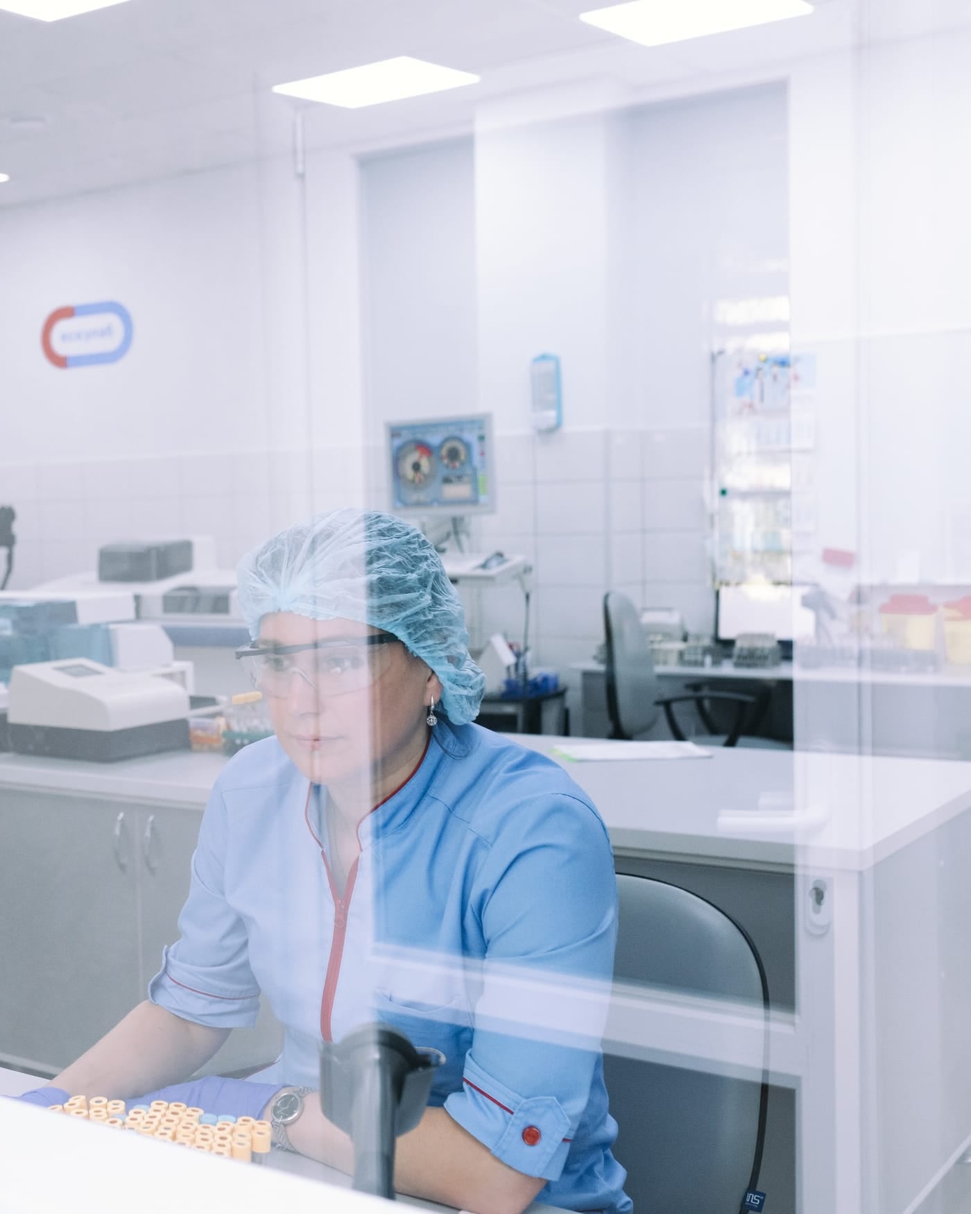 Scientist in a cap and blue scrubs working at a bench in a bright white medical laboratory