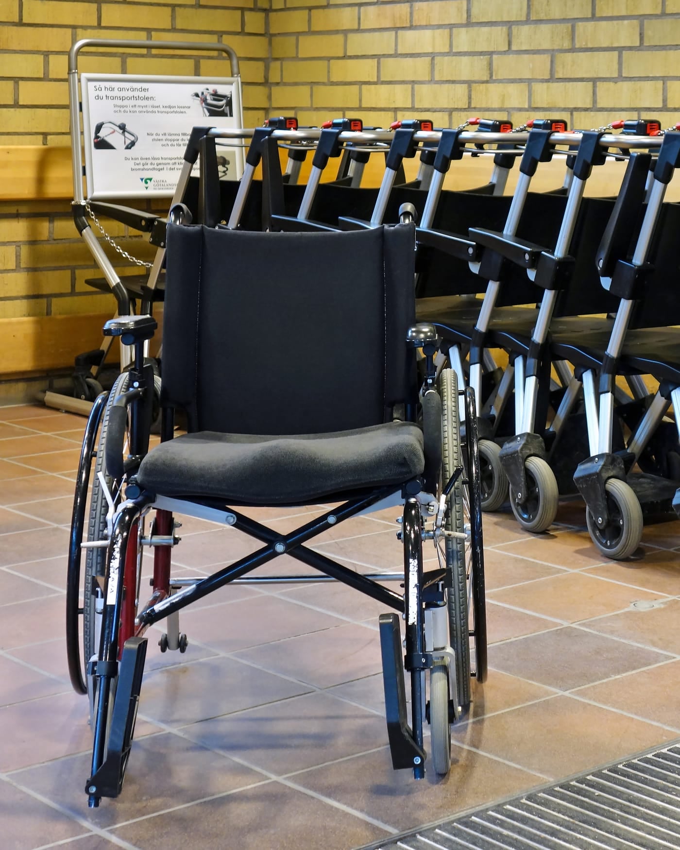 Row of folded wheelchairs lined up against a yellow brick wall at a hospital entrance