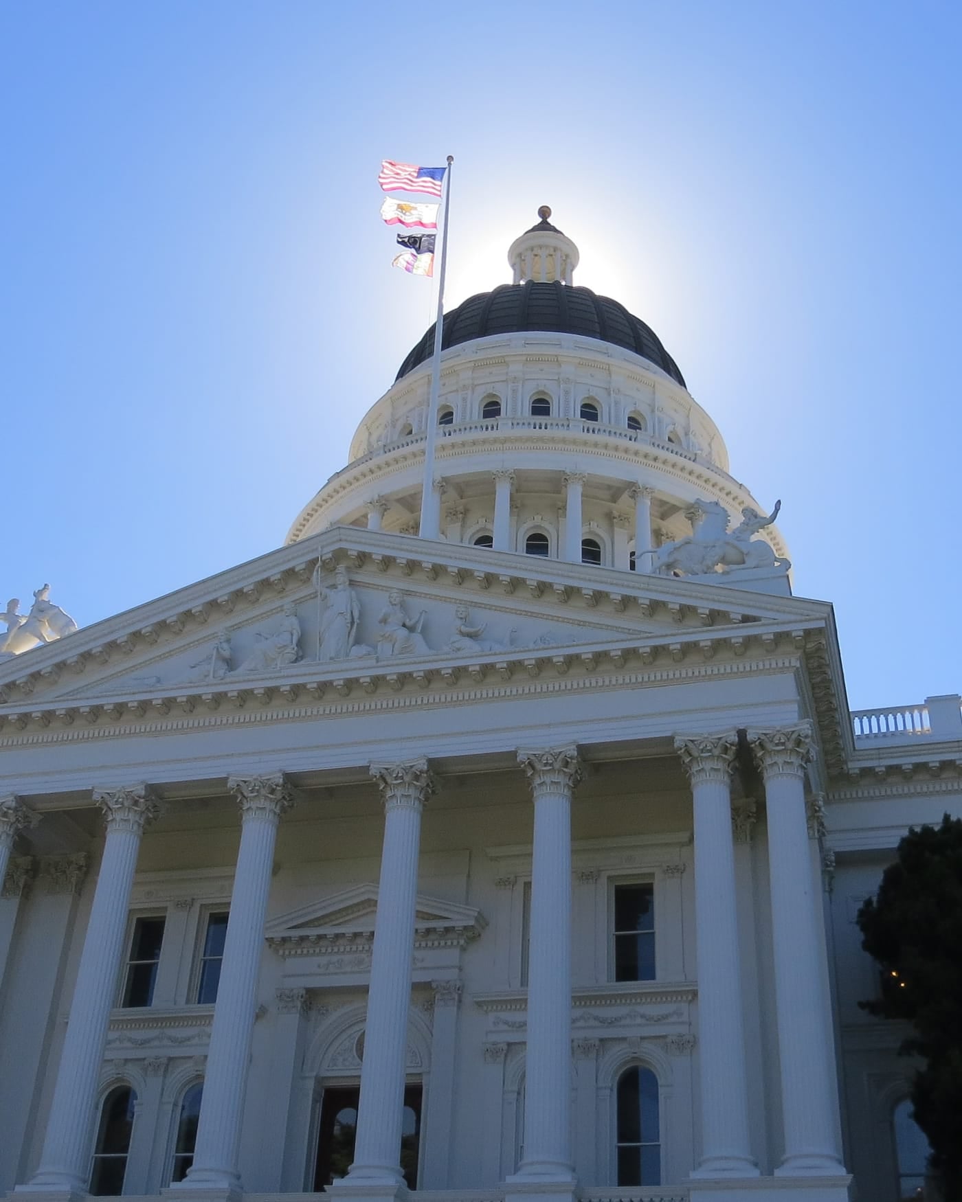 White dome and columned facade of the California State Capitol in Sacramento under a bright sky