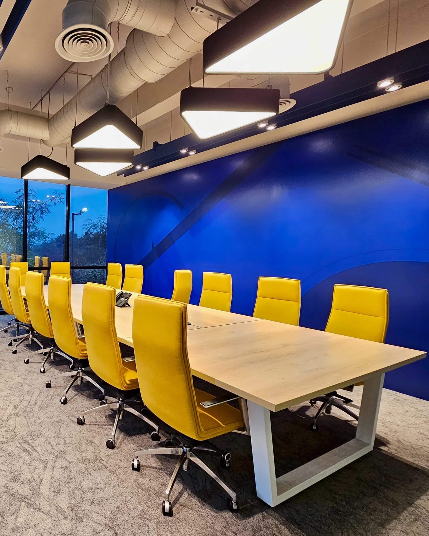 Modern conference room with a long wooden table, yellow chairs and a blue wall at dusk
