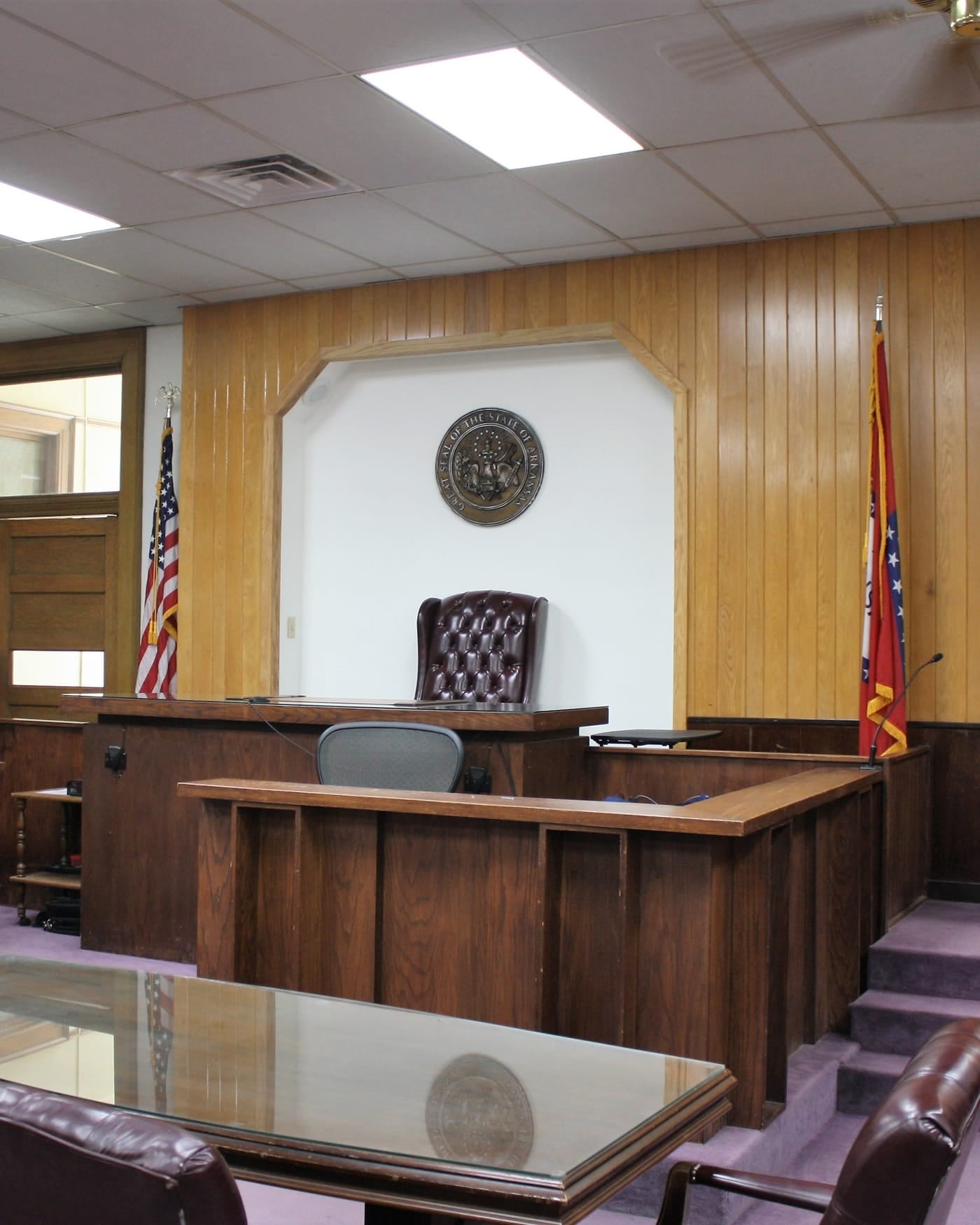Wood-paneled county courtroom with judge's bench, witness stand and flags