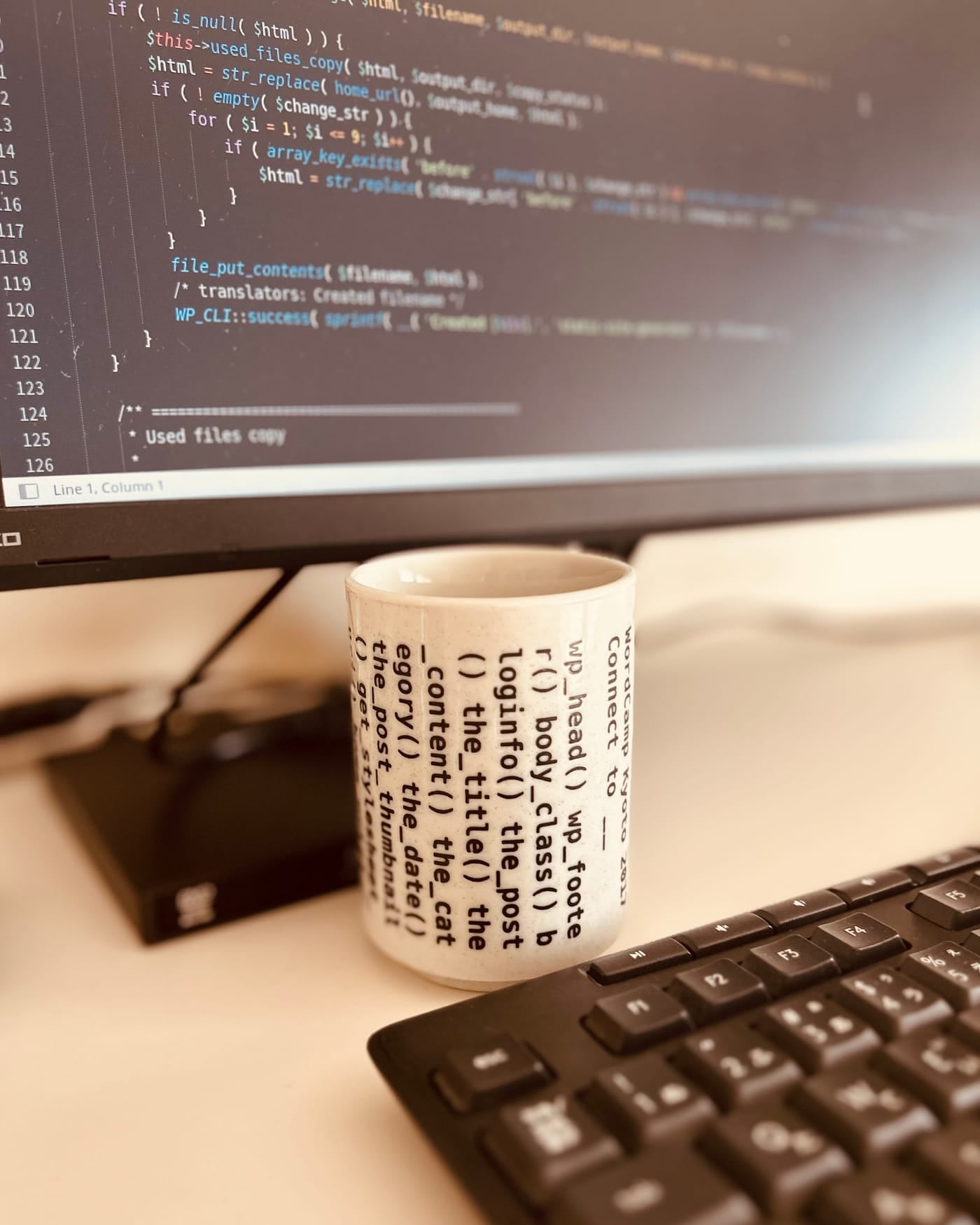 Desktop monitor showing PHP code behind a code-printed teacup and a black keyboard
