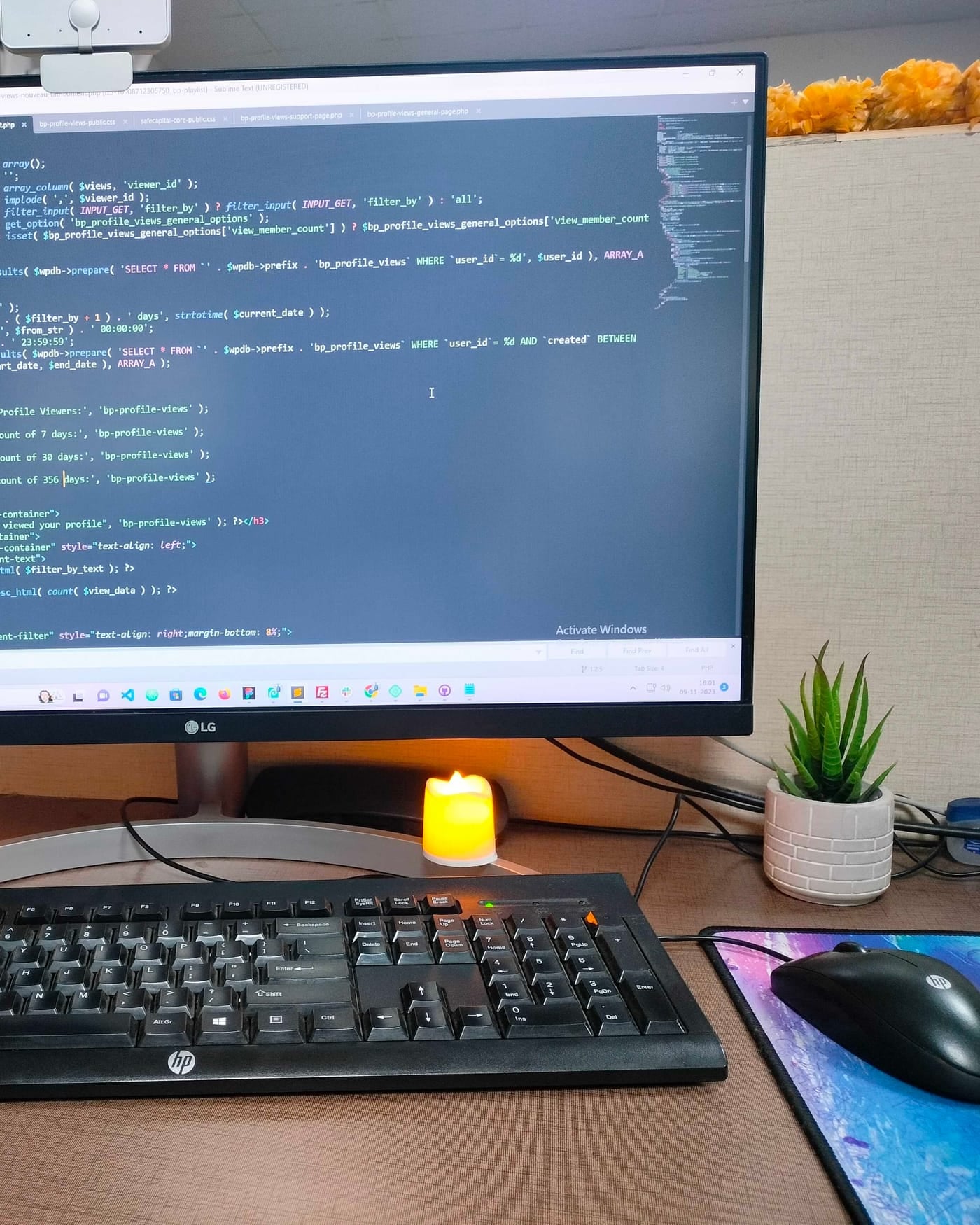 Desktop monitor displaying web code on a desk with two candles and a small plant