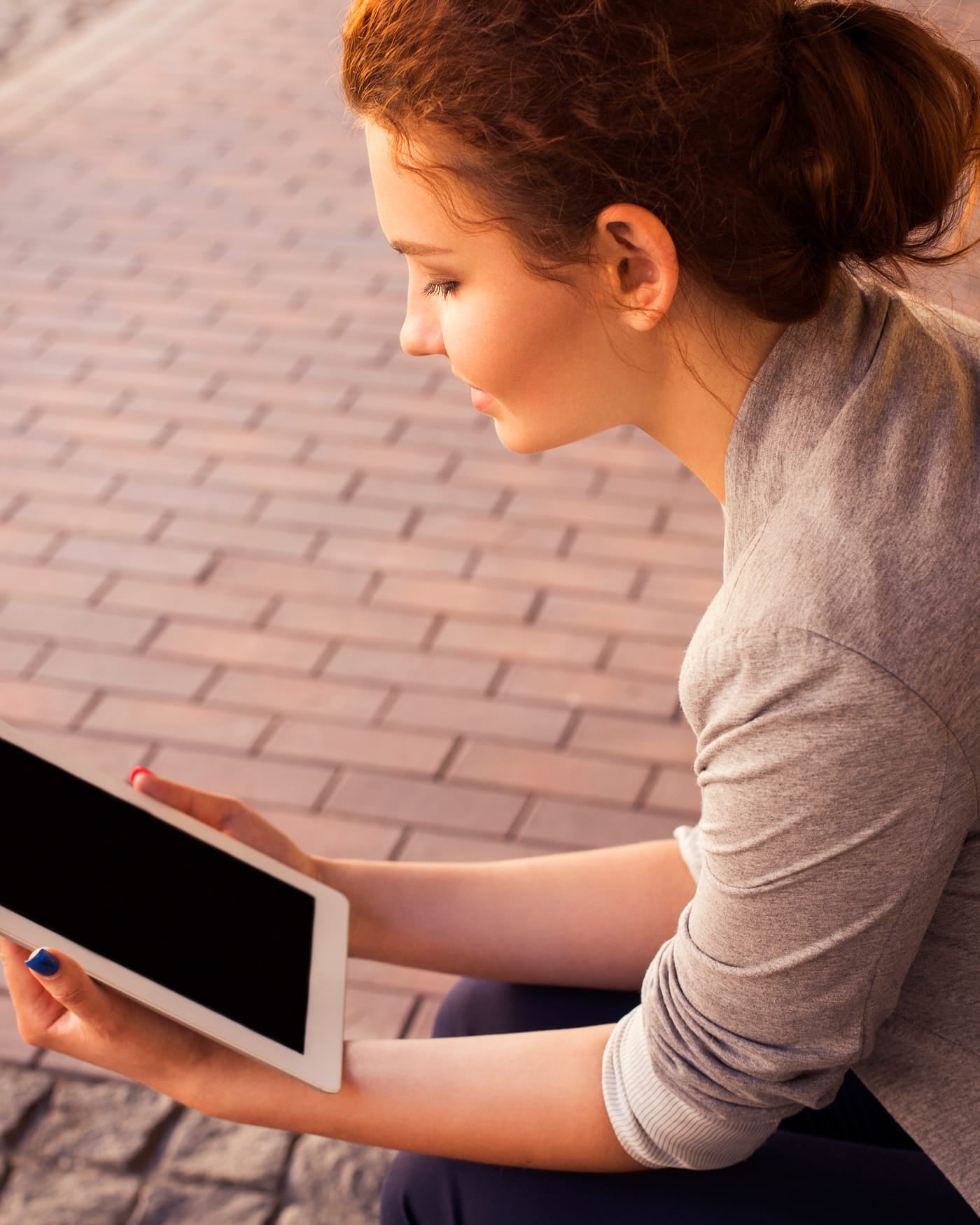 Woman seated on a brick walkway holding a tablet in her lap