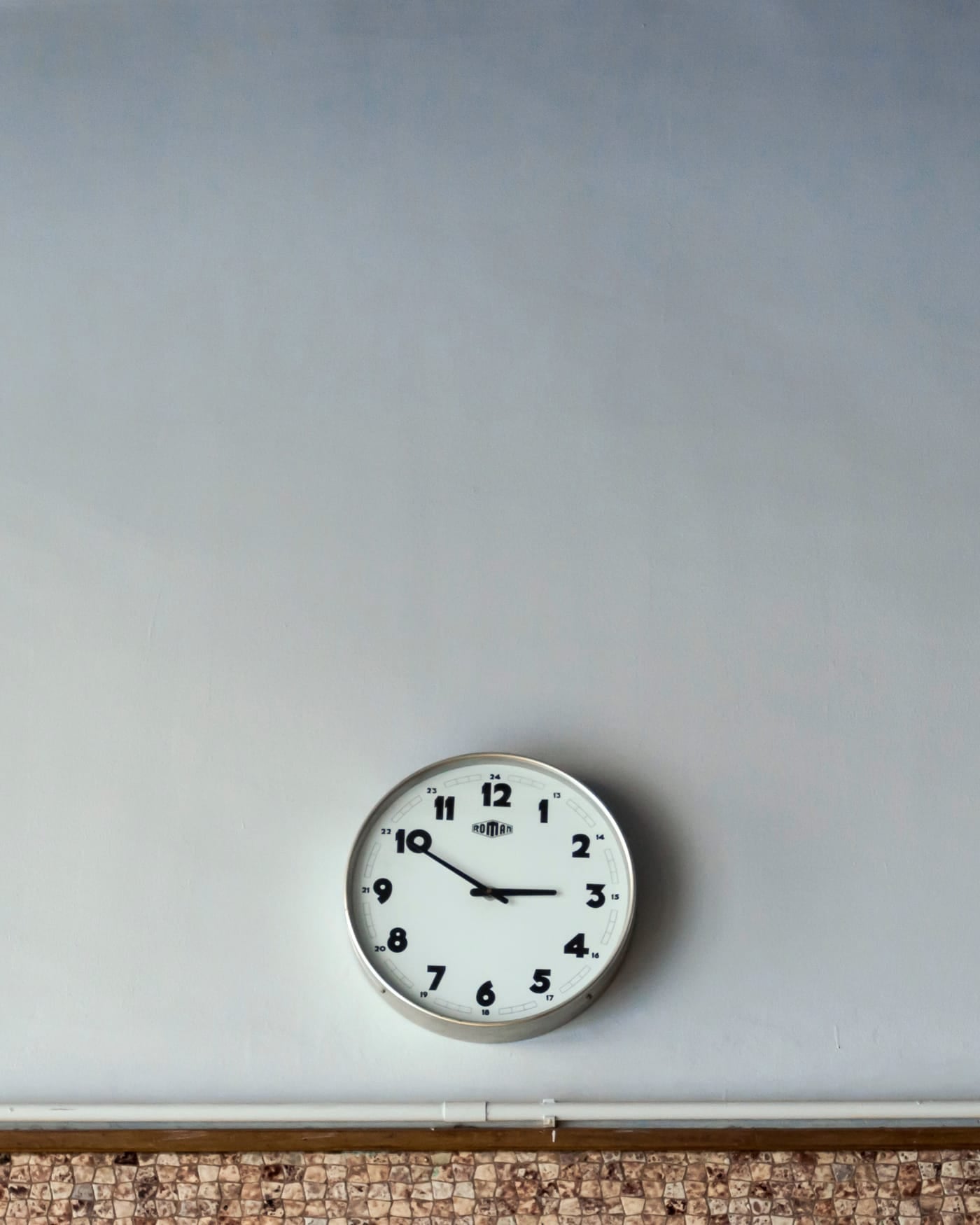 Small round analog wall clock on a plain pale wall