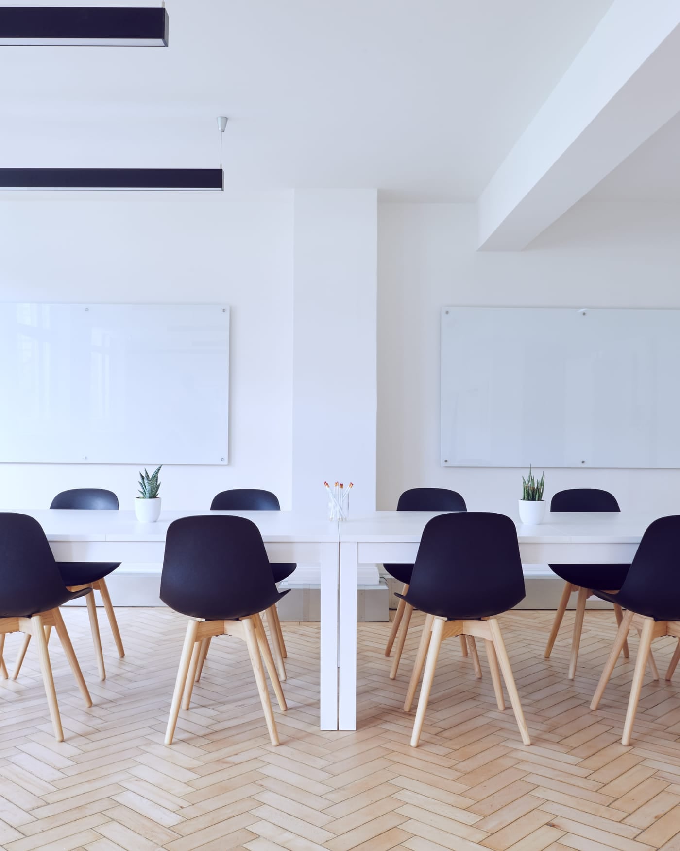 Bright white conference room with a long table, black chairs and a wall-mounted screen