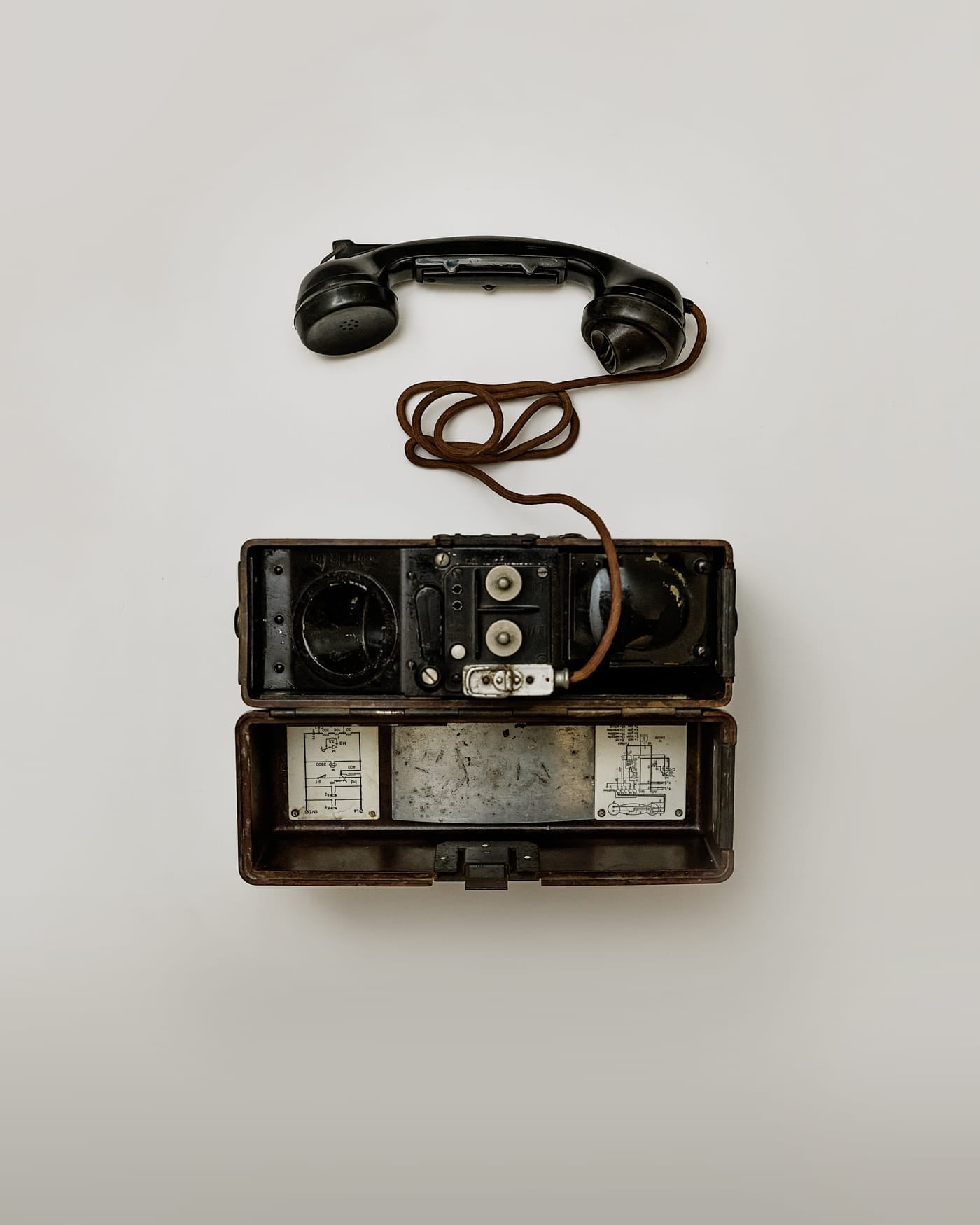 Antique black wall telephone with a hanging handset on a pale grey wall