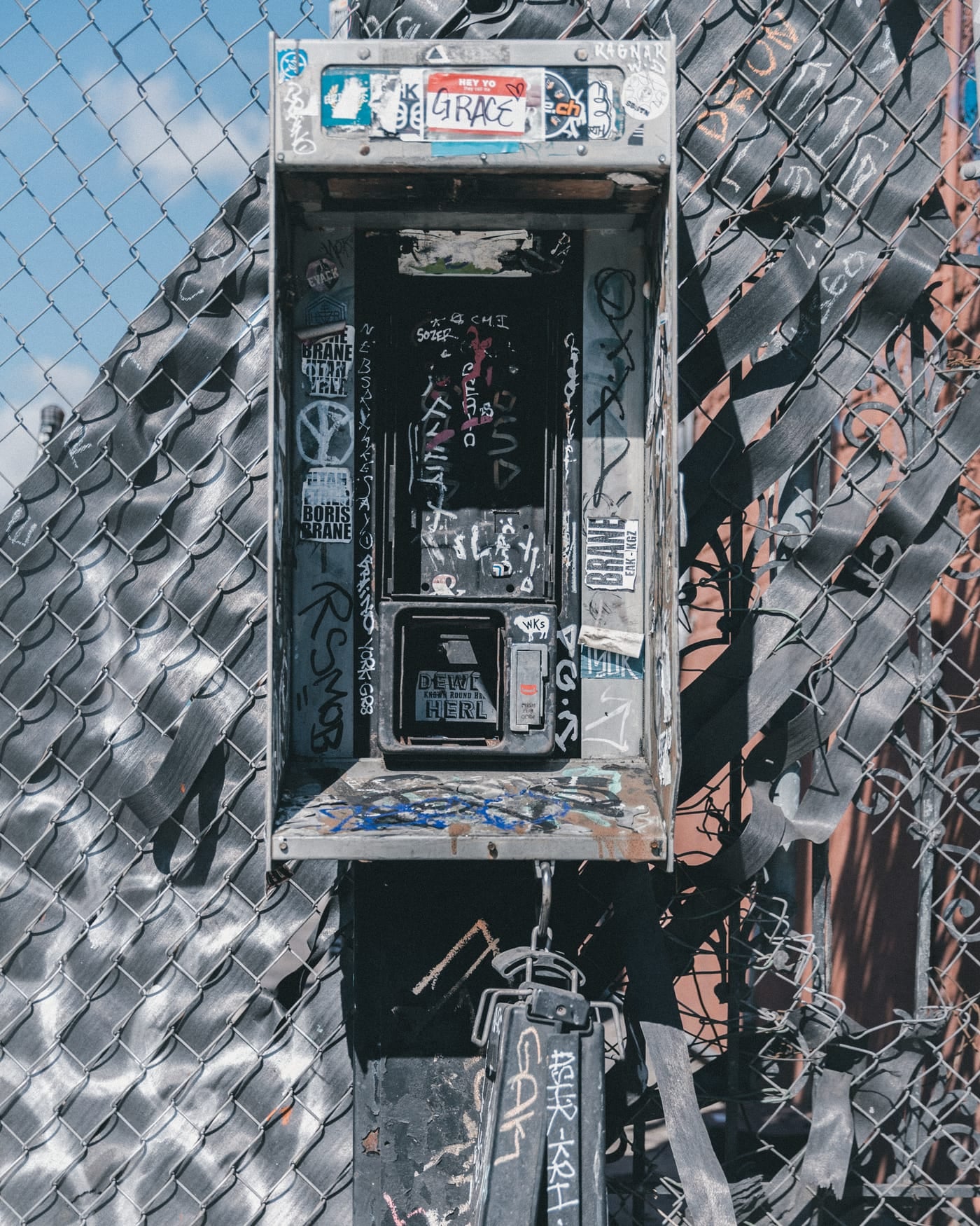Old payphone set into a graffiti-covered wall behind a chain-link fence
