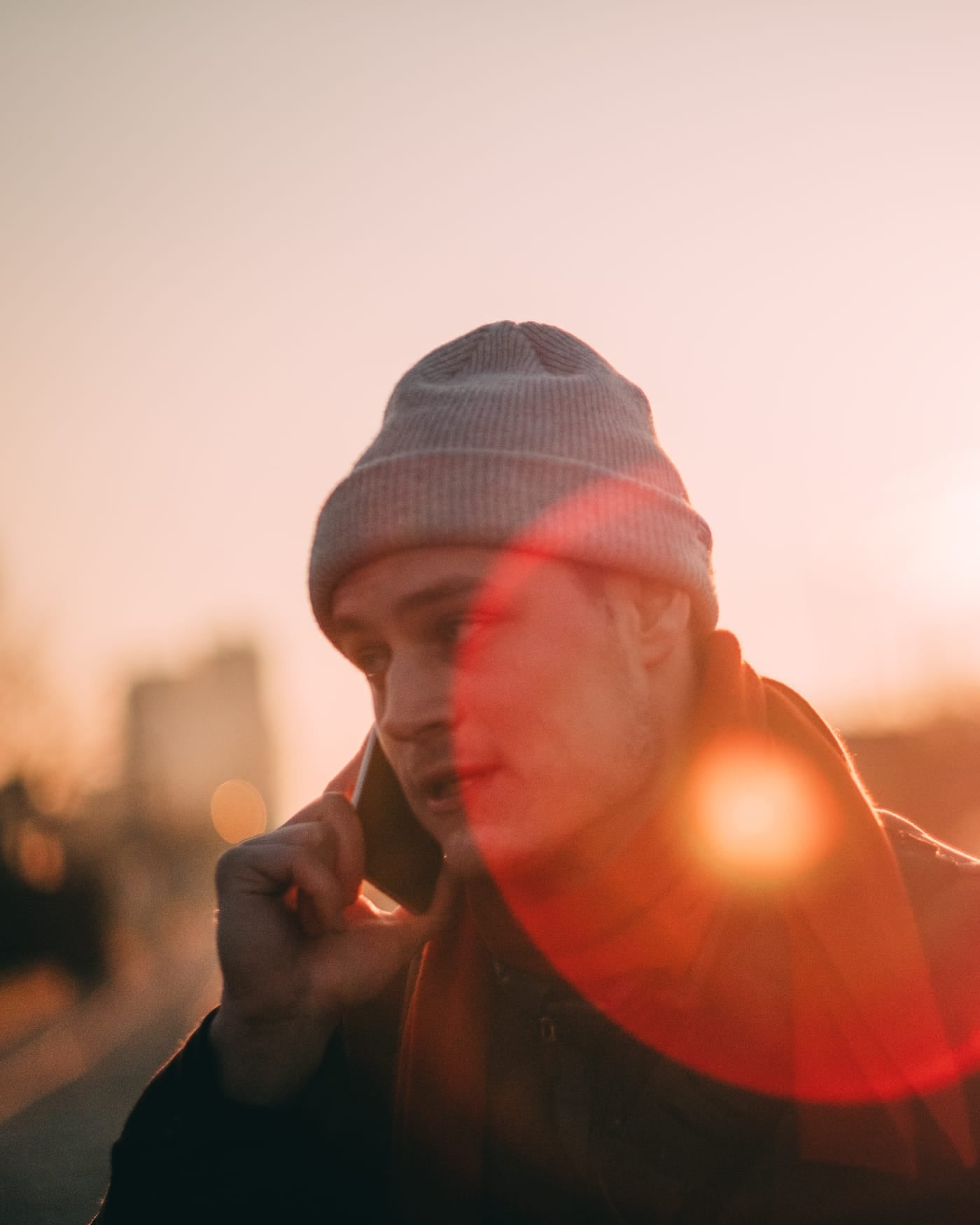 Man in a knit cap talking on a phone at sunset with warm lens flare
