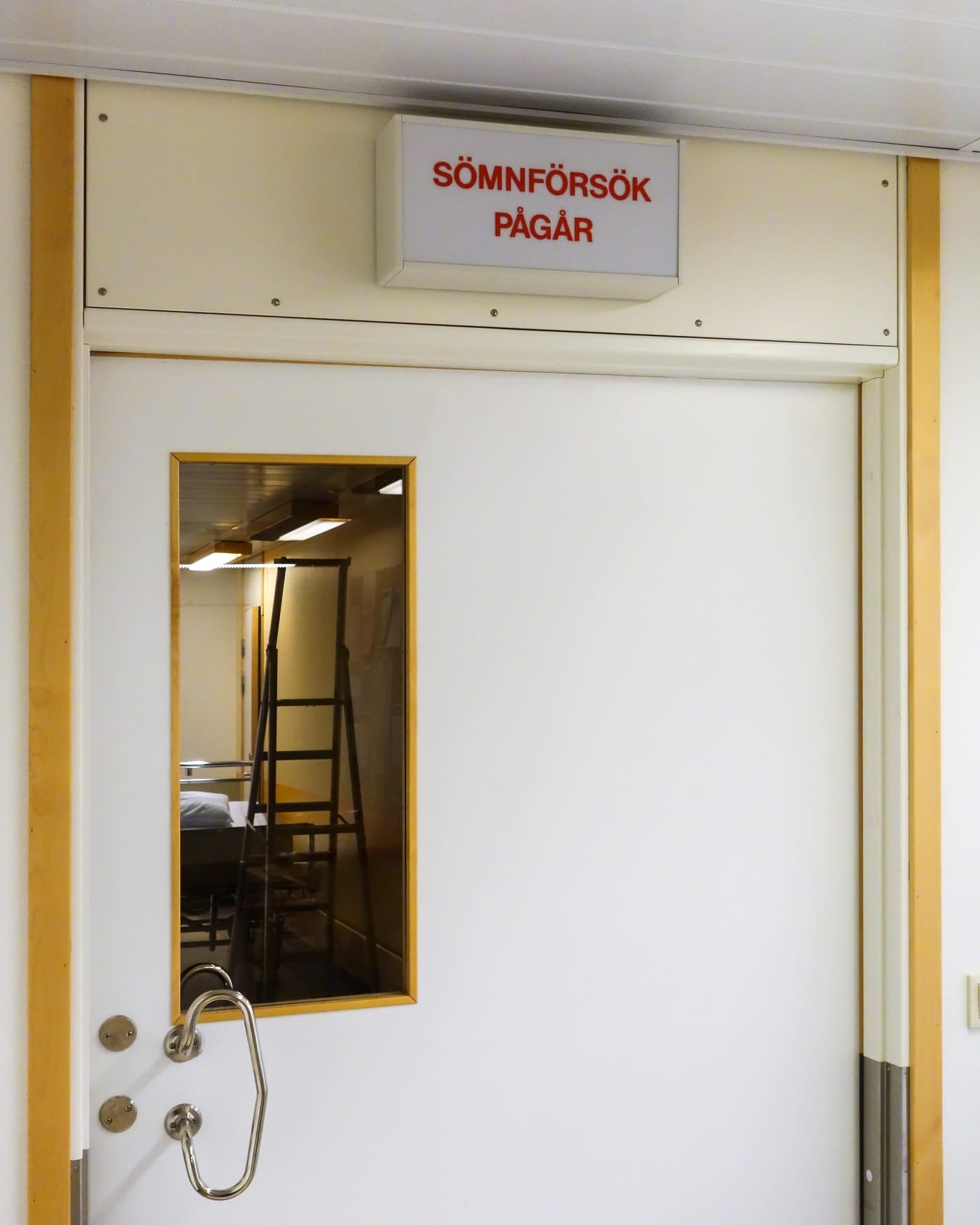 Closed white hospital door with a small window and a red 'study in progress' sign above it