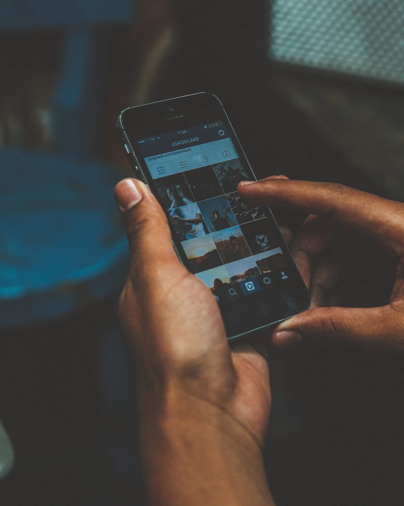 Two hands holding a smartphone in dim blue light, thumb touching the screen