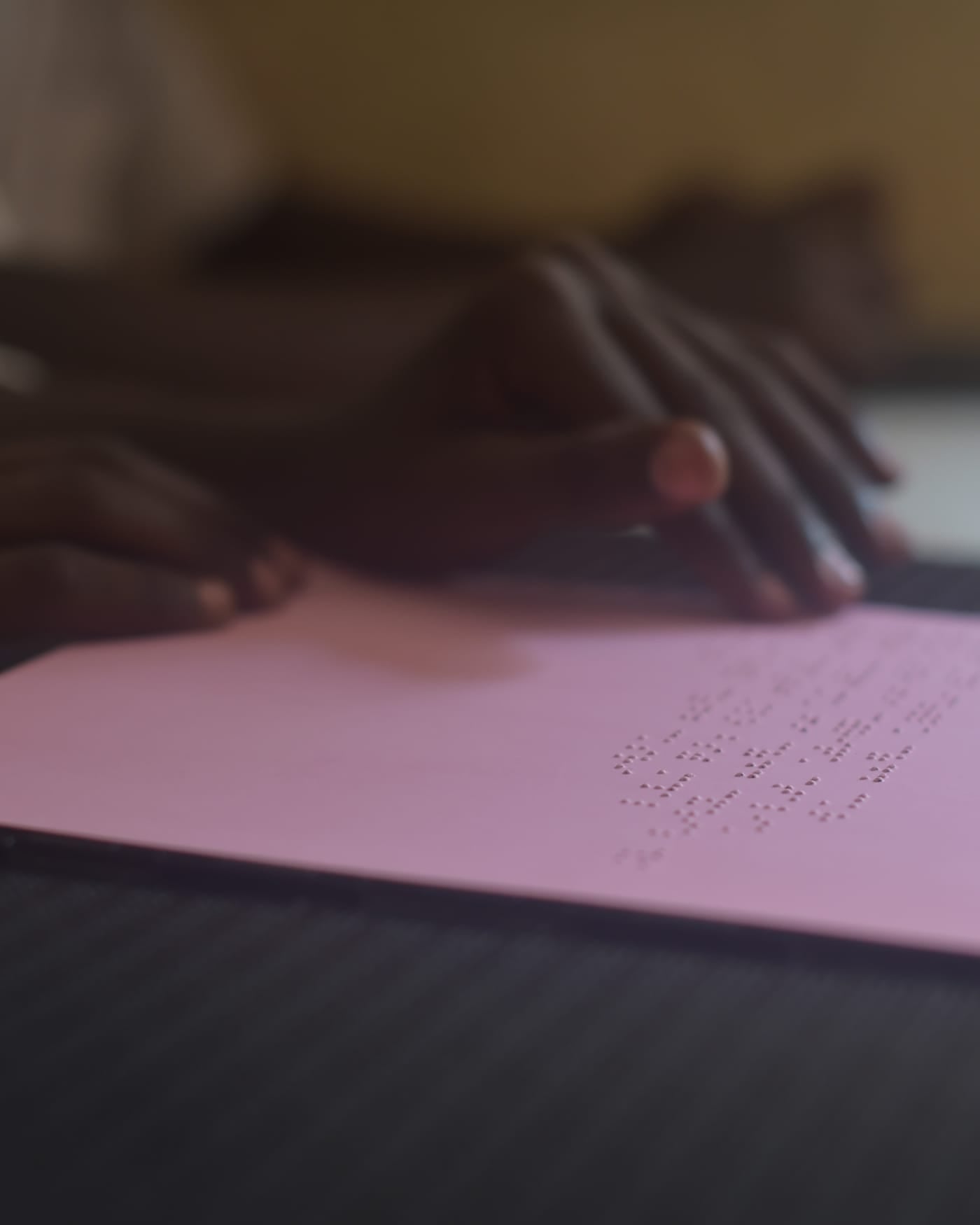 Hands reading a pink braille sheet on a school desk