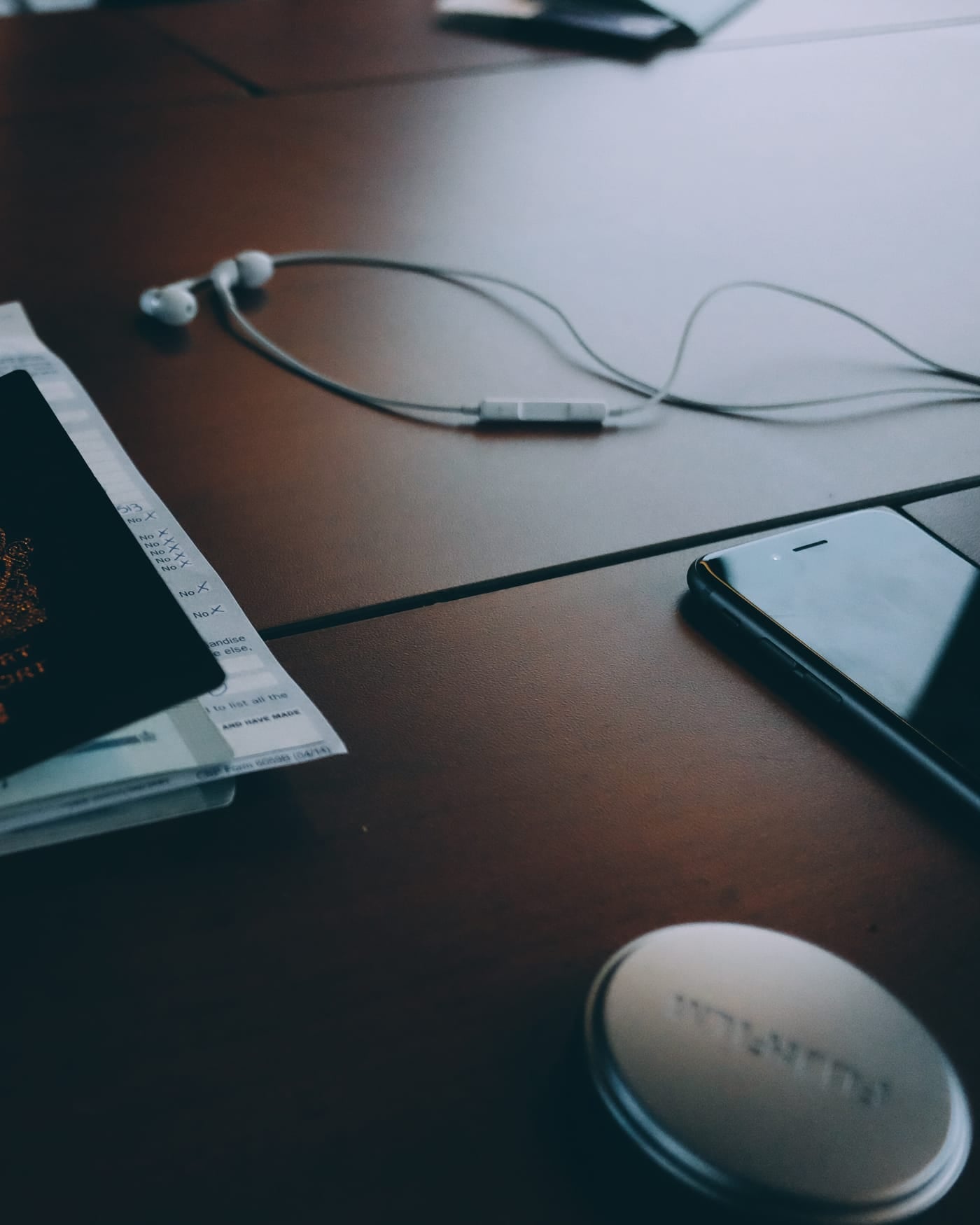 Passport and travel documents on a dark wooden desk beside a phone and earphones