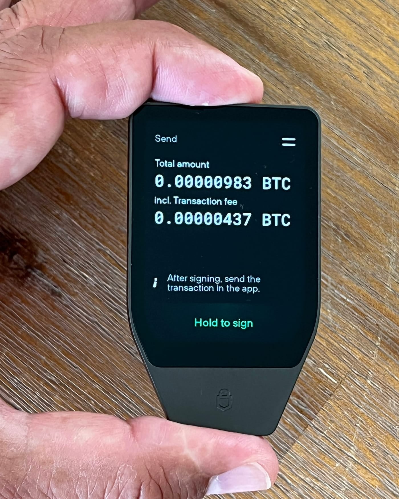 Hand holding a hardware crypto wallet showing a bitcoin send transaction on its screen