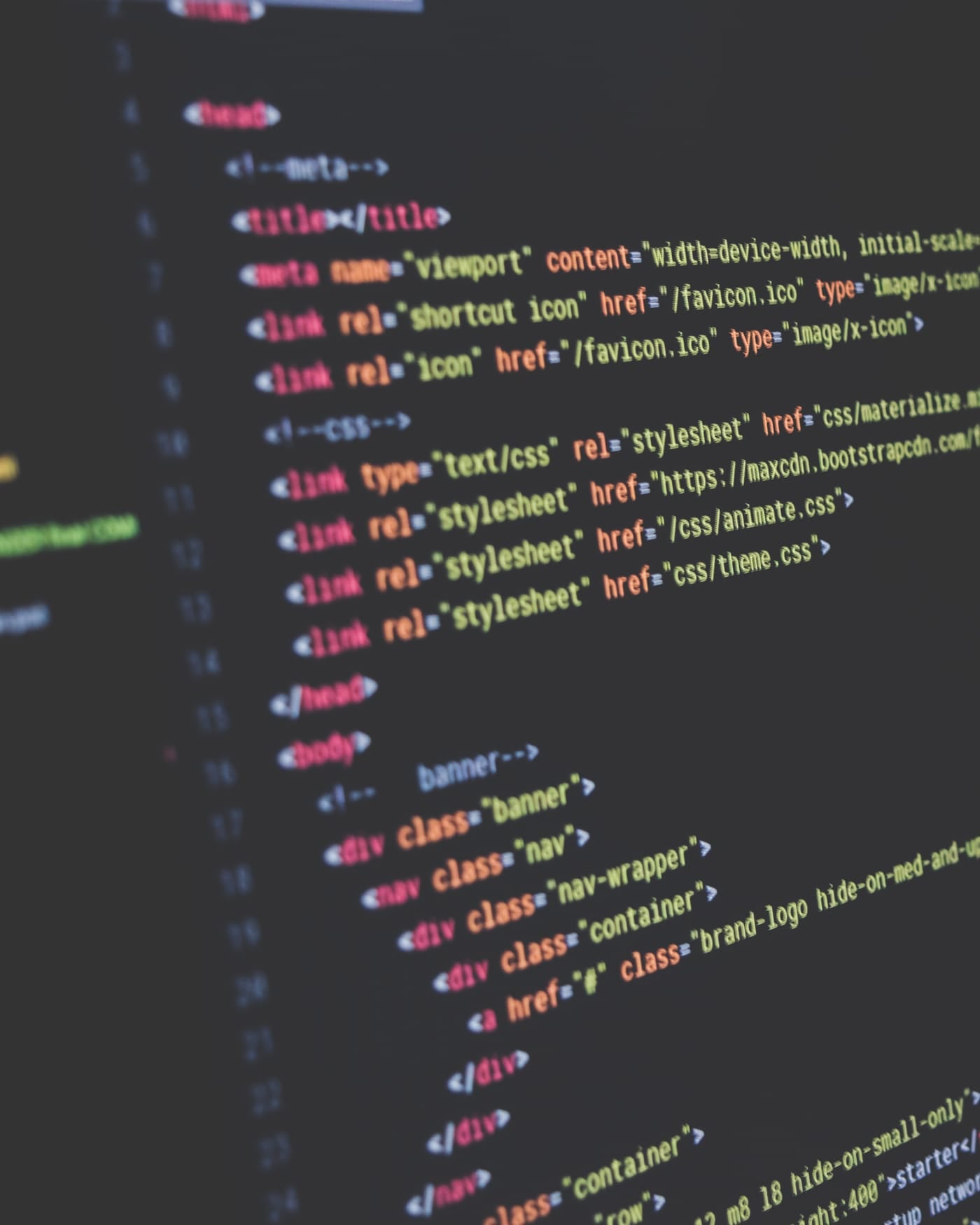 Lines of colored source code on a dark monitor with a blurred app window behind