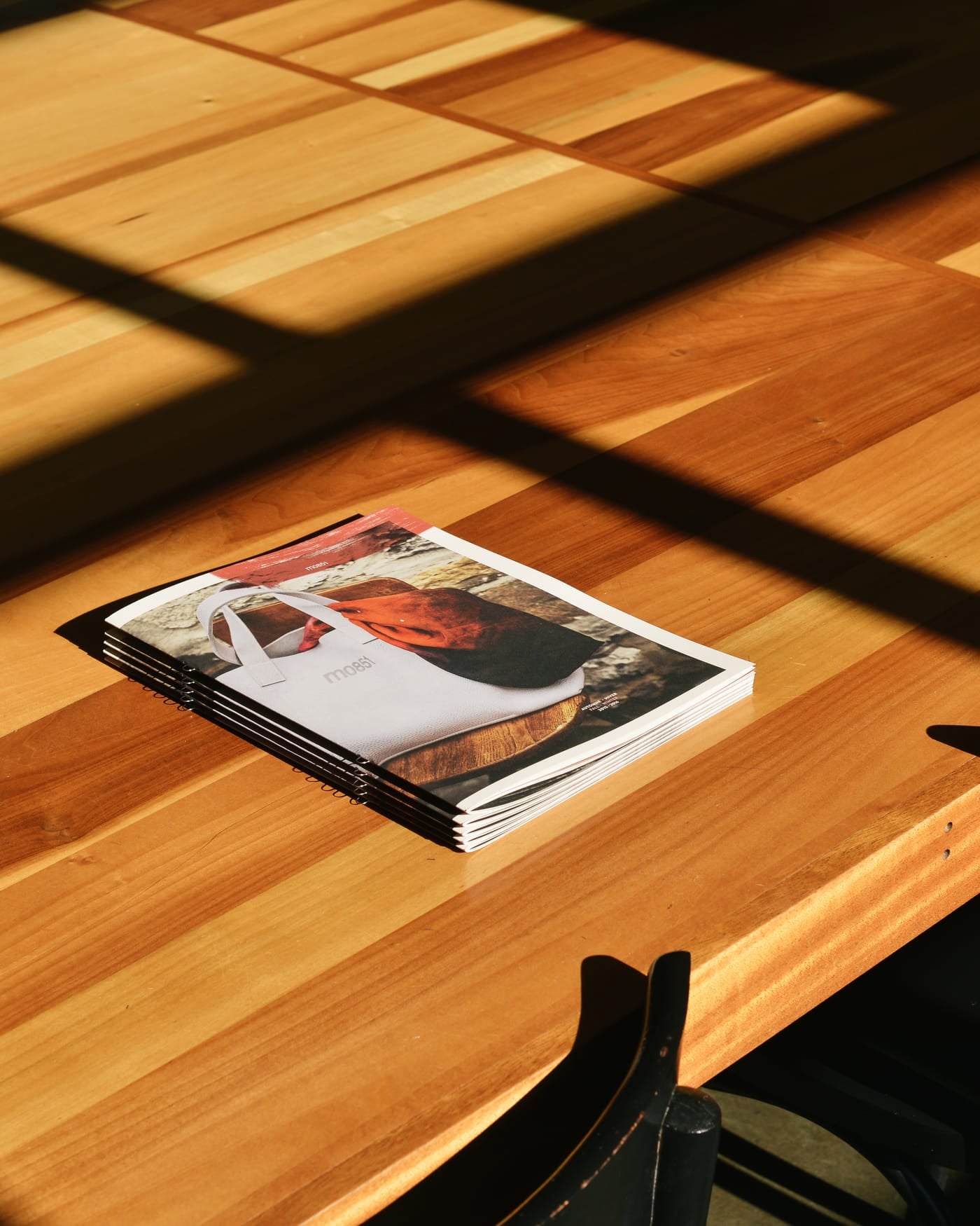 Stack of printed magazines on a wooden table in strong window light