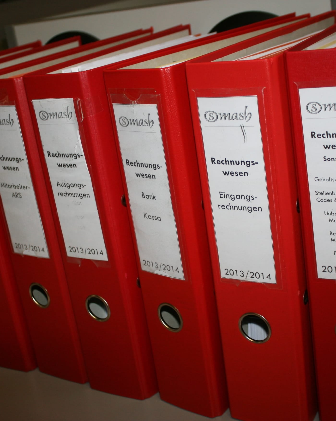 Row of red lever-arch binders with printed labels on an office shelf