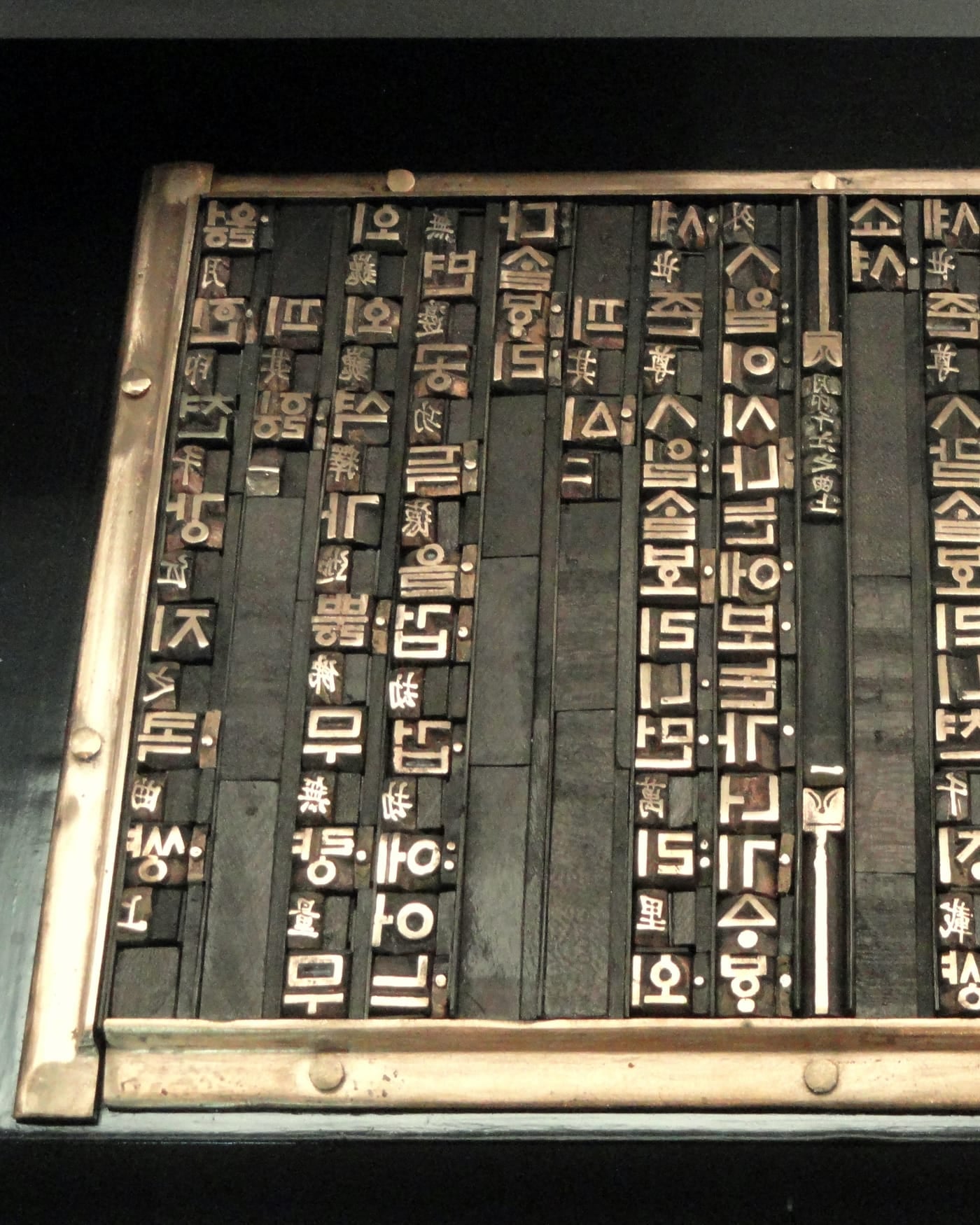Tray of metal Korean movable type sorted in rows on a dark background