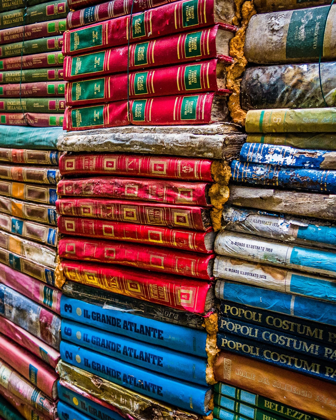 Wall of colourful stacked hardback books with red, blue and gold spines