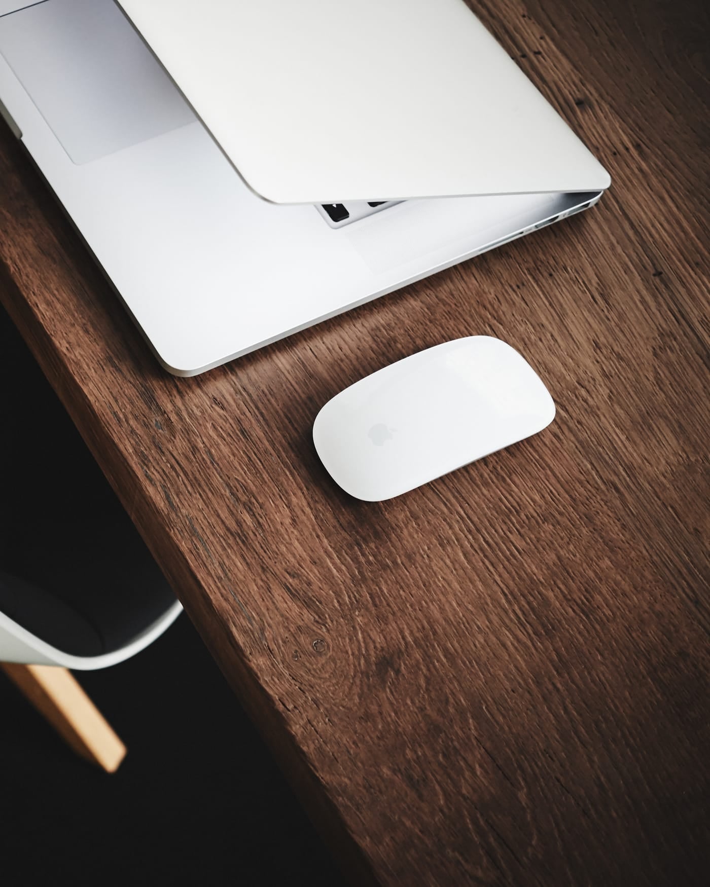 Half-closed silver laptop and mouse on a dark wooden desk