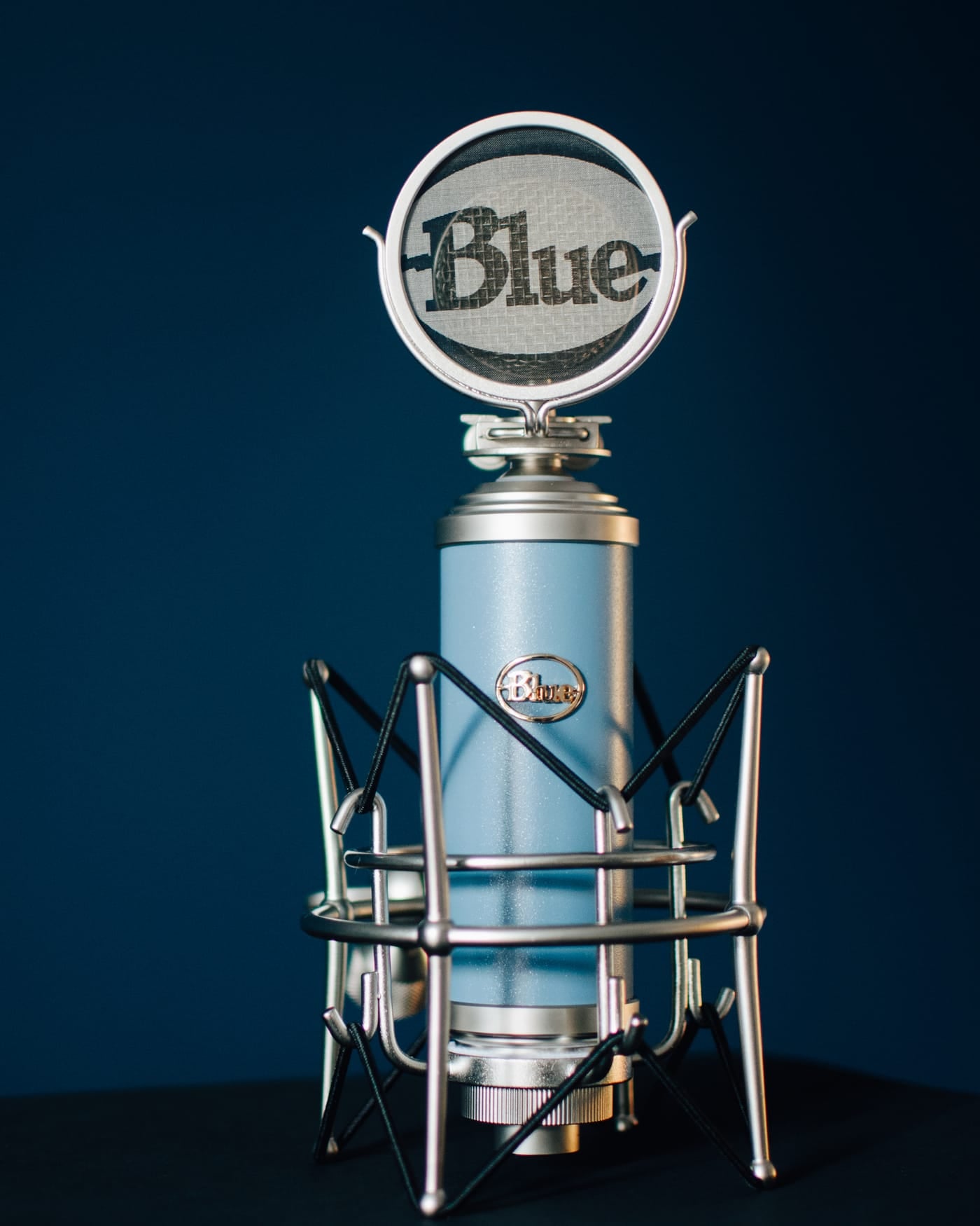 Blue condenser microphone in a shock mount against a dark background