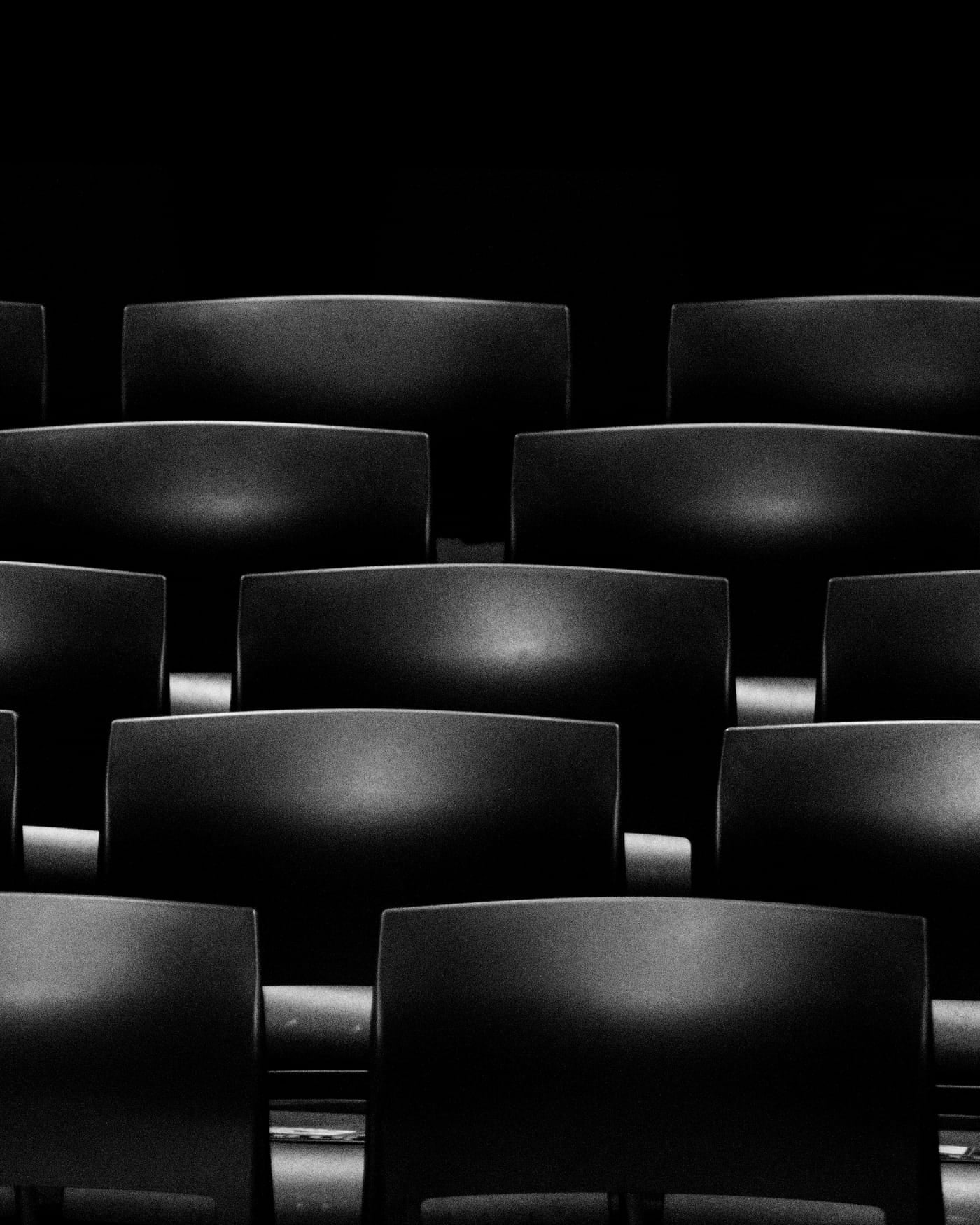 Rows of empty black cinema seats in a dark theater