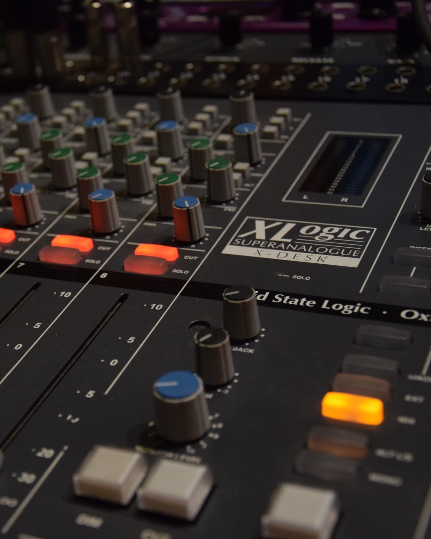 Close-up of an analogue audio mixing console with knobs and lit buttons