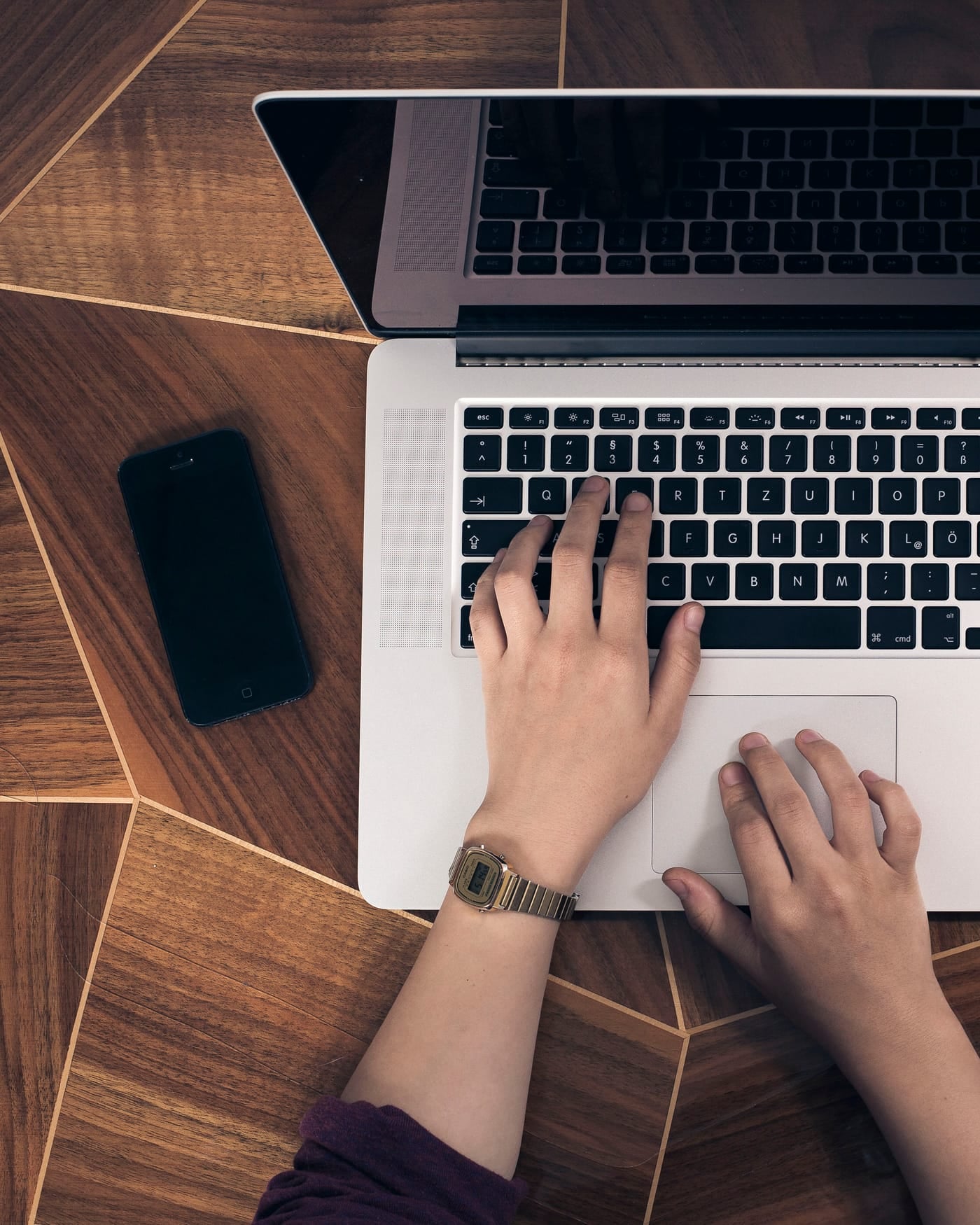 Hands typing on a laptop keyboard on a wooden desk, phone beside it