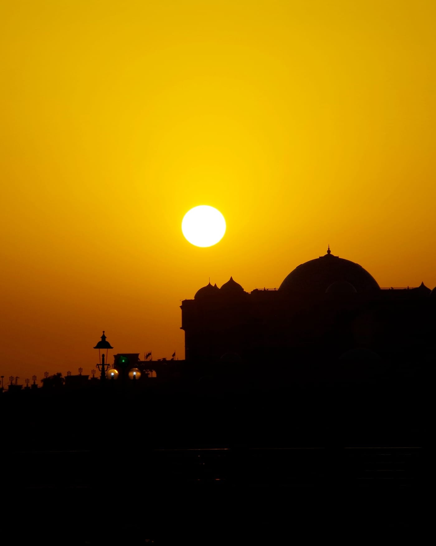Silhouette of a domed palace against an orange sunset sky in Abu Dhabi