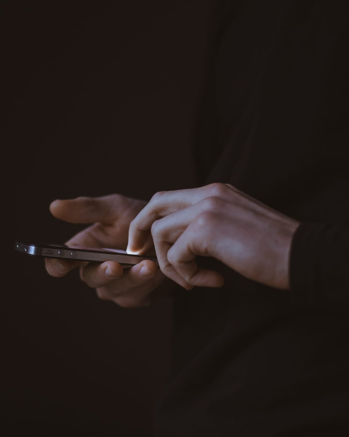 Hands typing on a smartphone in a dark room