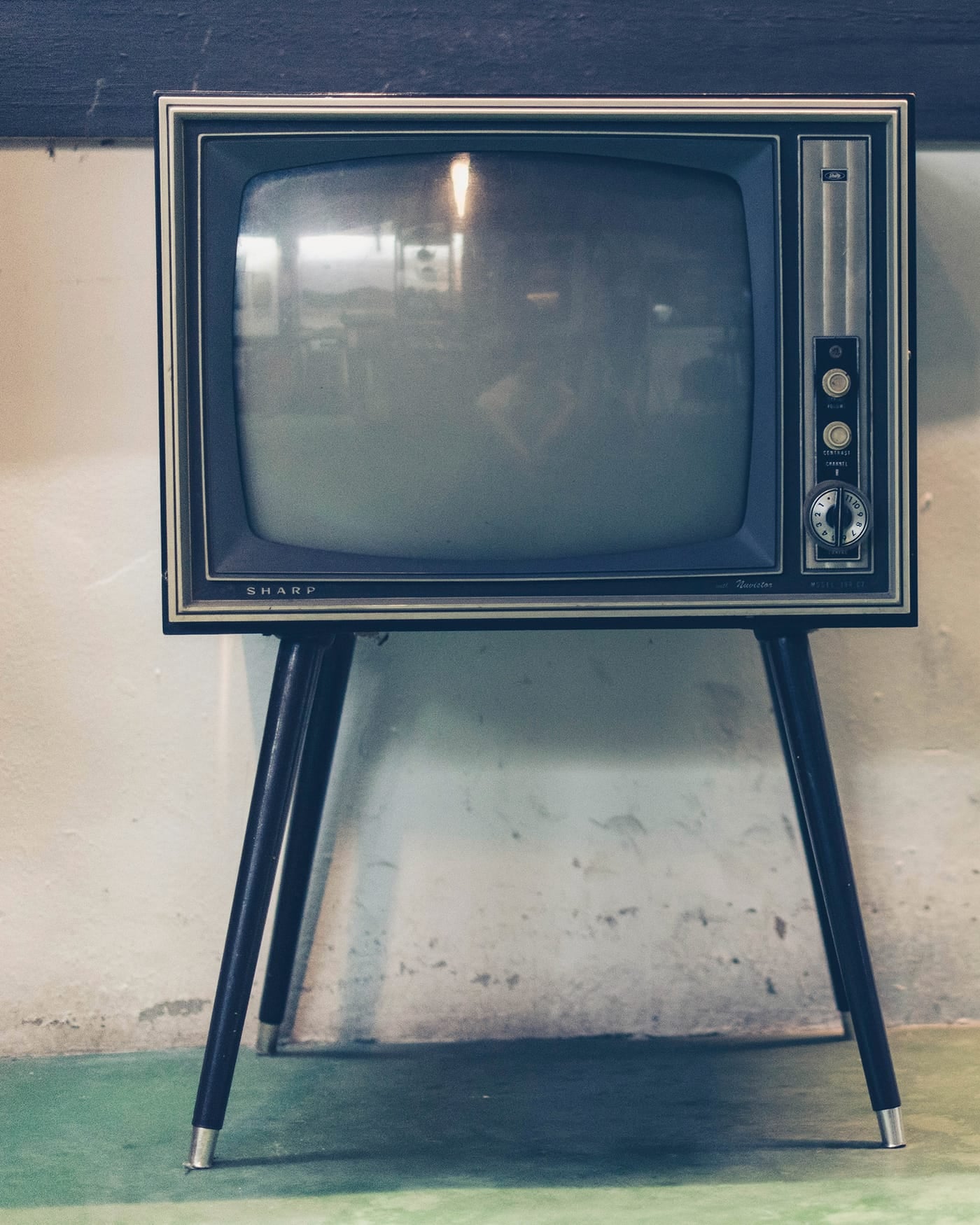 Vintage television set on thin legs standing against a plain wall