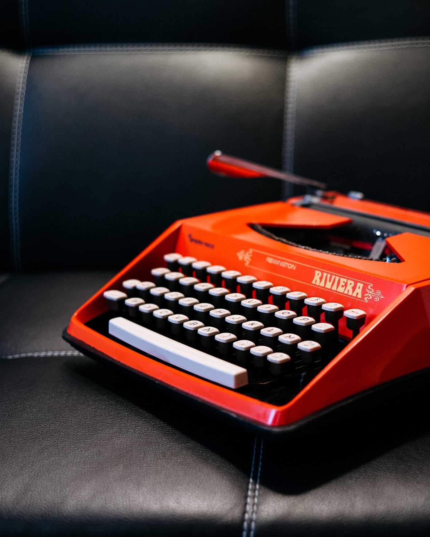 Bright red vintage typewriter on a black leather sofa
