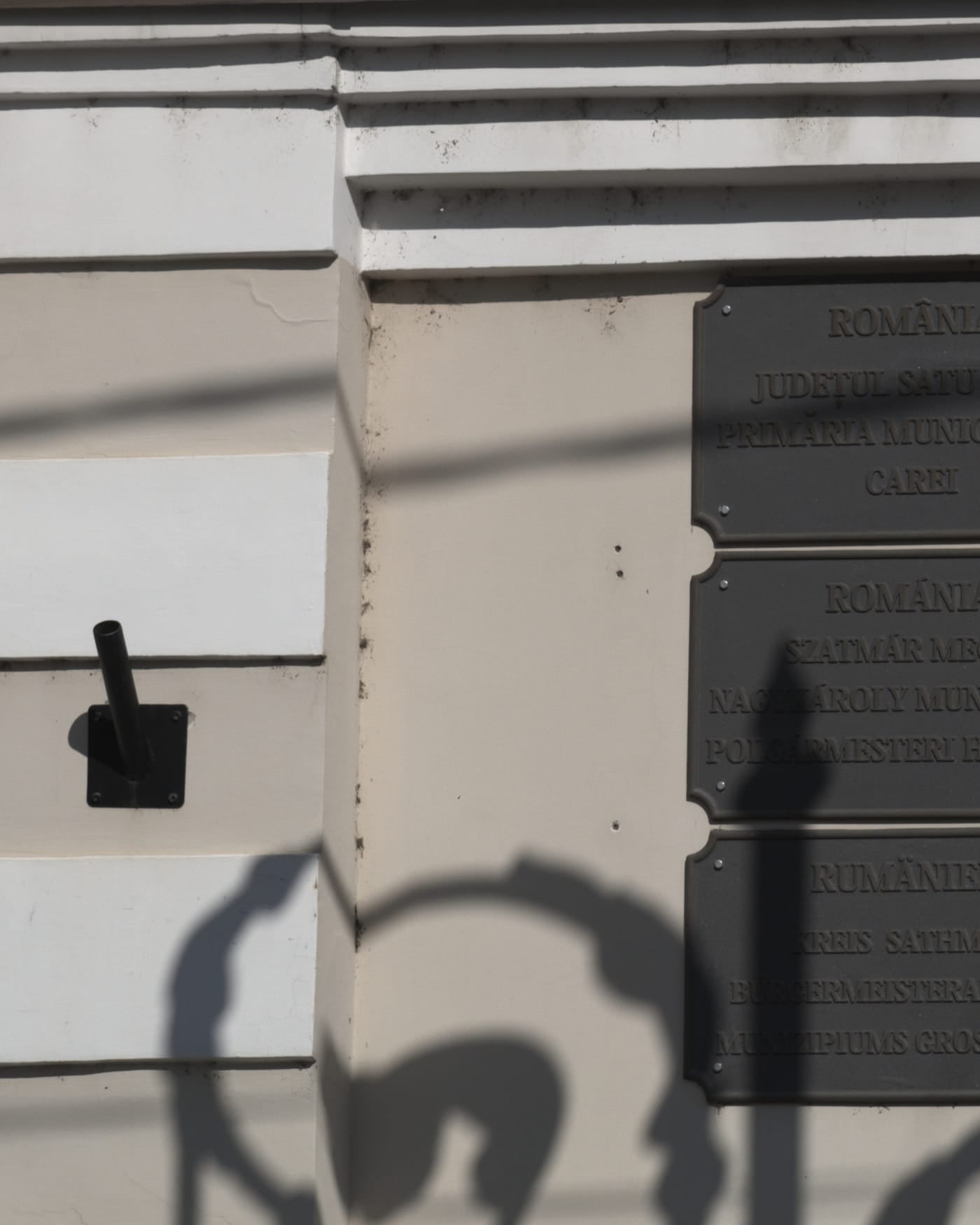 Sunlit wall with a column of engraved municipal plaques in several languages
