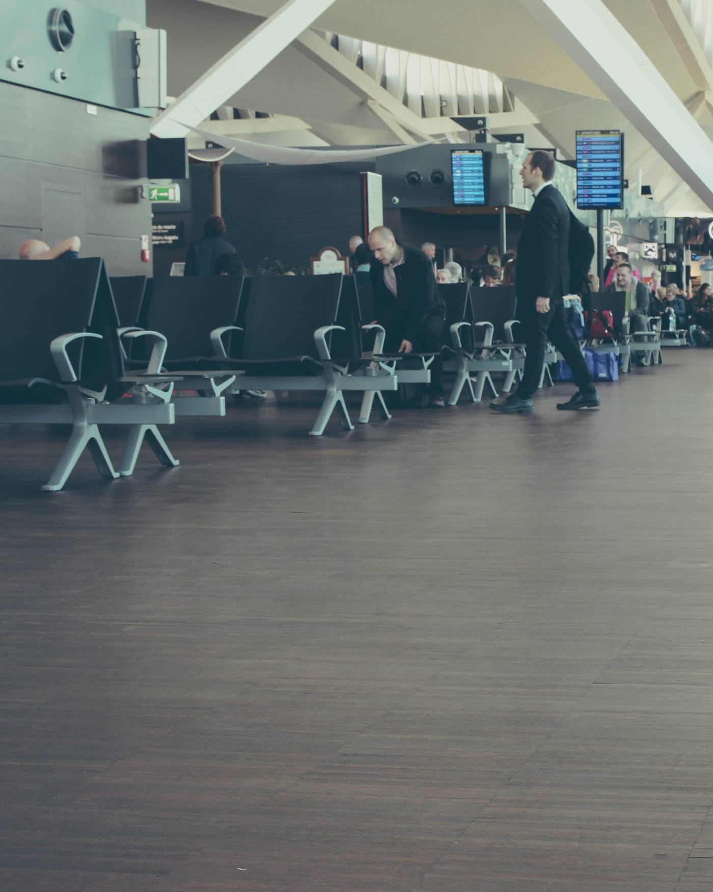 Airport departure hall with rows of seats and a traveller pulling a suitcase