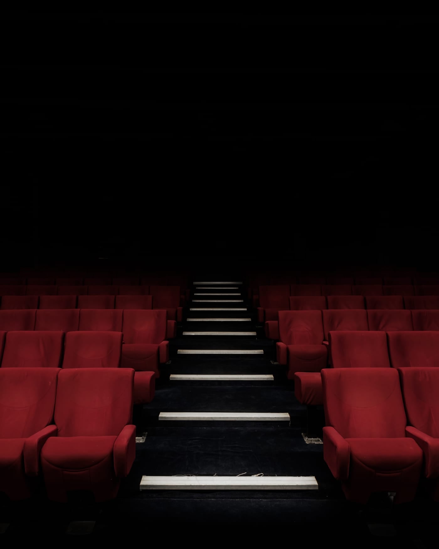 Rows of red cinema seats with a lit aisle in a dark auditorium