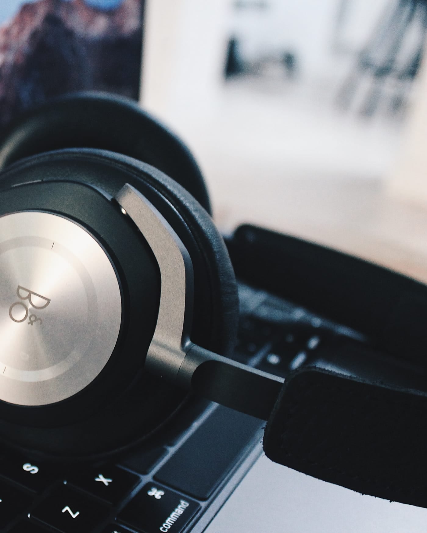 Over-ear headphones resting on a laptop keyboard with a mountain wallpaper on screen
