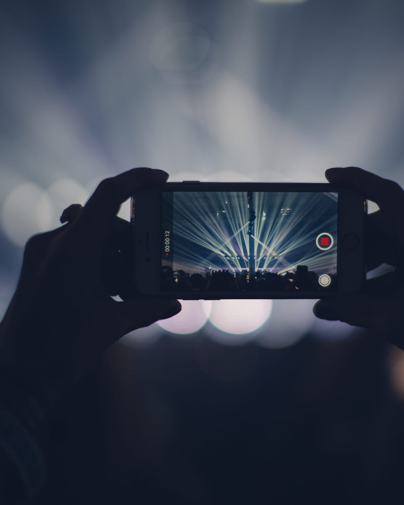 Hands holding up a smartphone to record a stage lit by blue concert lights