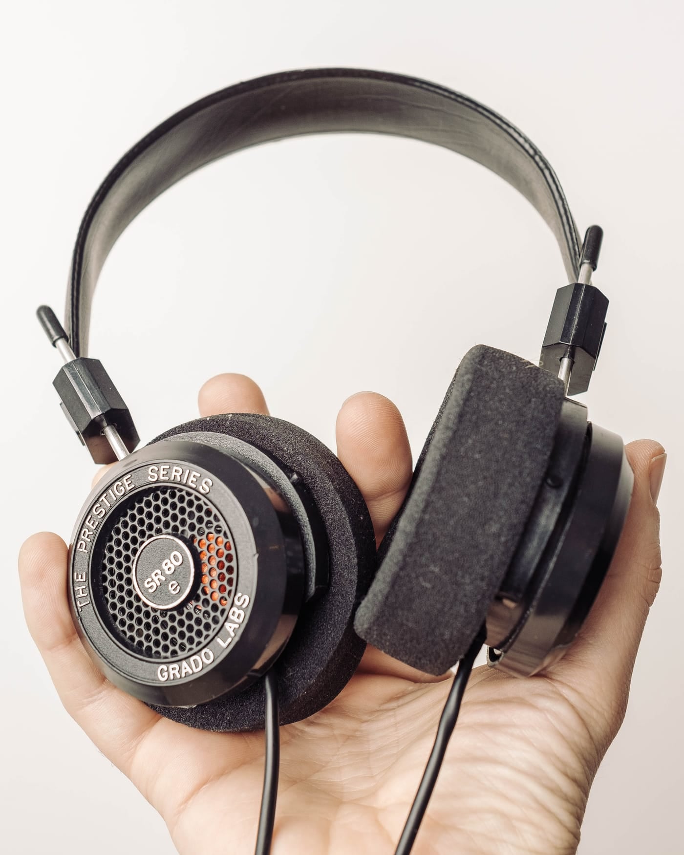 Hand holding a pair of open-back Grado headphones against a white background
