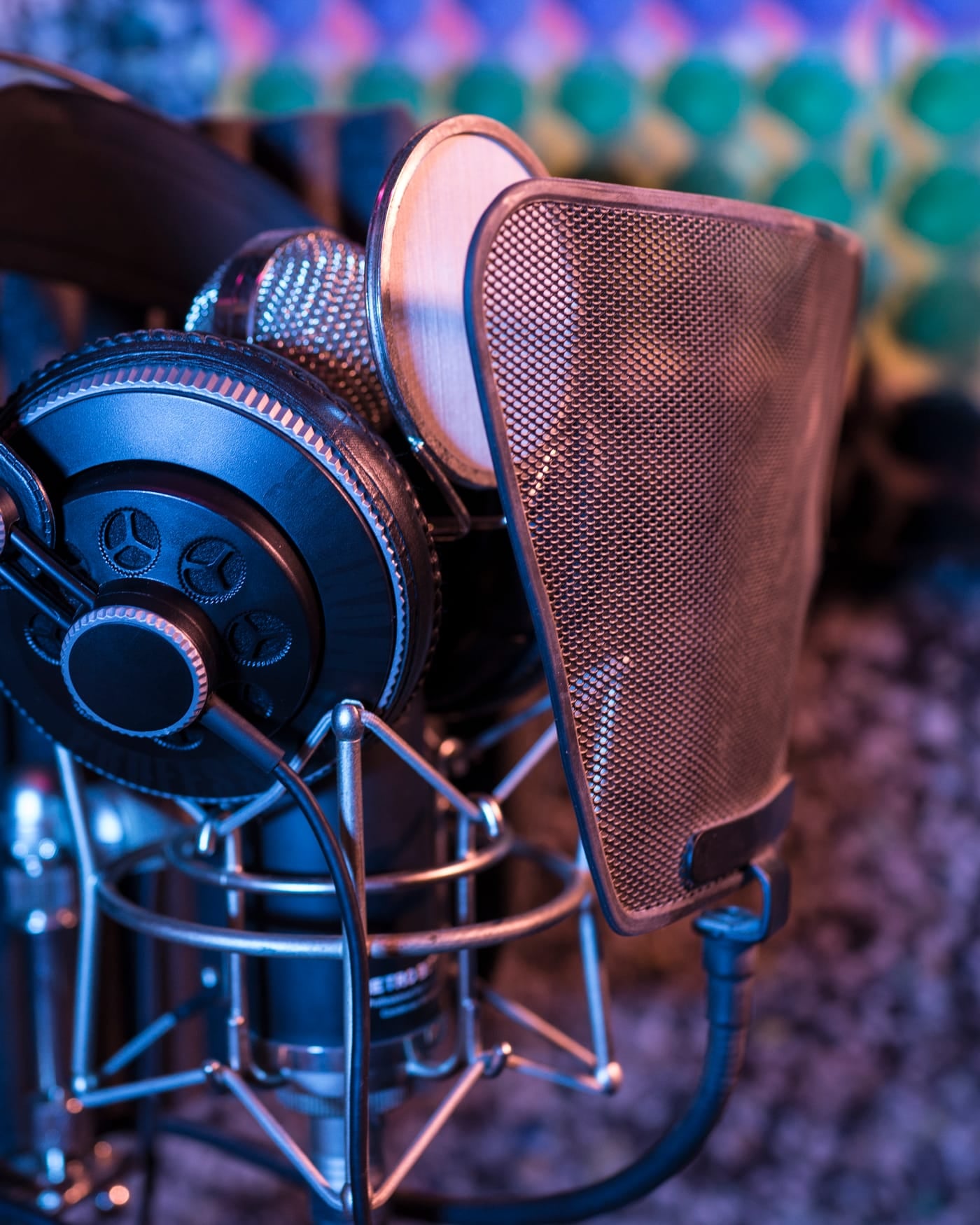 Studio condenser microphone with a pop filter and headphones, lit in blue and amber