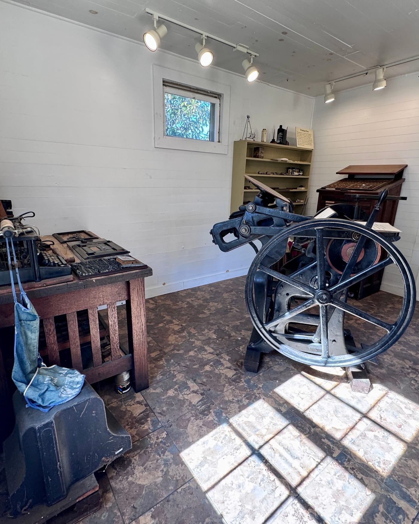 Antique iron hand printing press with a large flywheel in a sunlit white print shop
