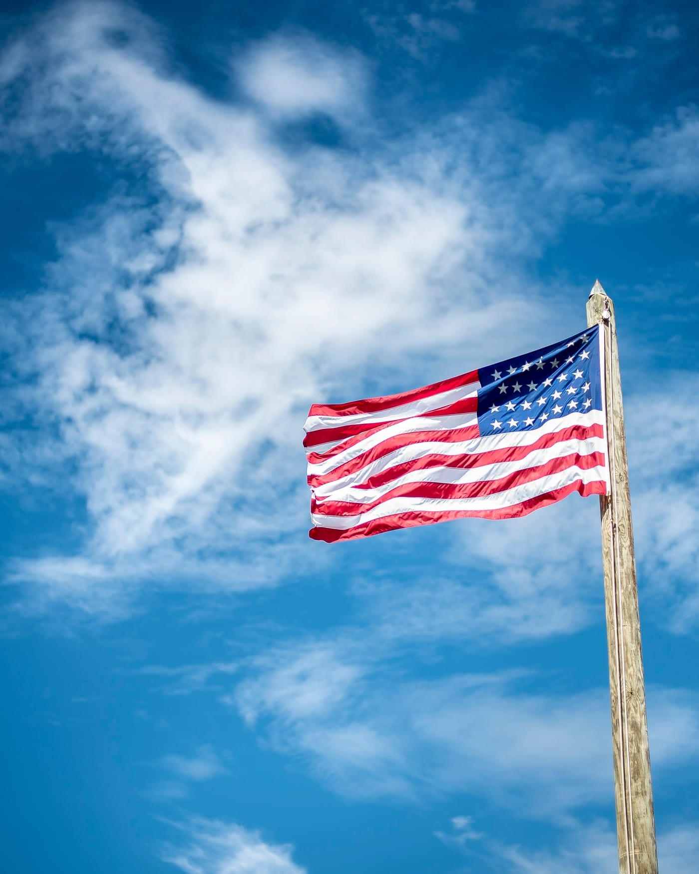 American flag flying from a wooden pole against a blue sky with scattered clouds