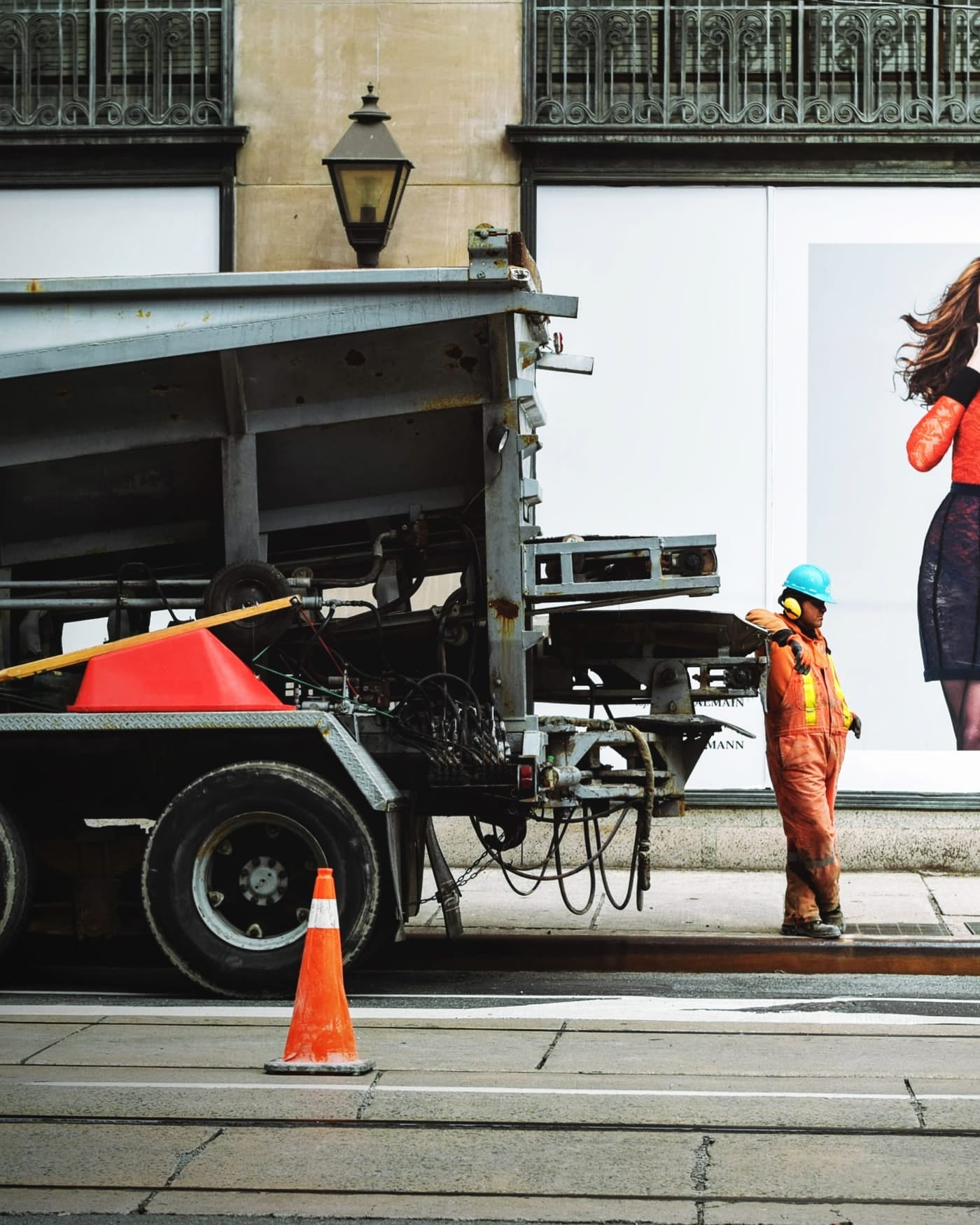 Worker in orange hi-vis overalls and a hard hat beside a lorry on a city street